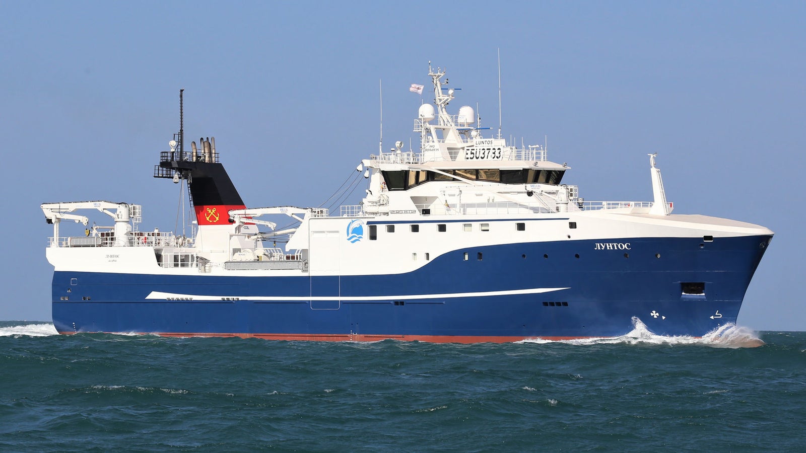 Prodotto - Peschereccio Luntos: Vista laterale della nave operativa in navigazione, scafo blu e bianco, attrezzature avanzate sul ponte, numero identificativo SU 073 visibile sulla sovrastruttura, ambiente marittimo sereno.