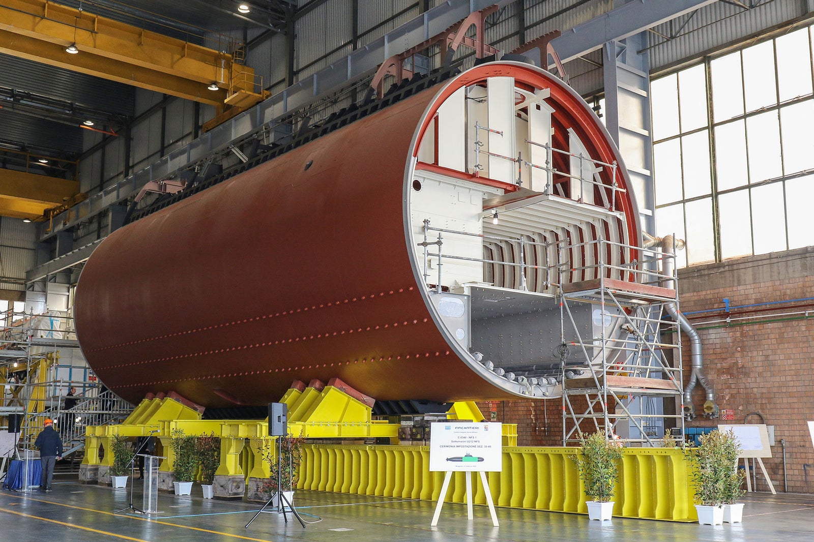 Newsroom - Press releases - 2026 - Fincantieri Group: keel-laying of the first U212NFS submarine at Muggiano: submarine hull section on yellow supports inside Muggiano shipyard, surrounded by scaffolding and plants.