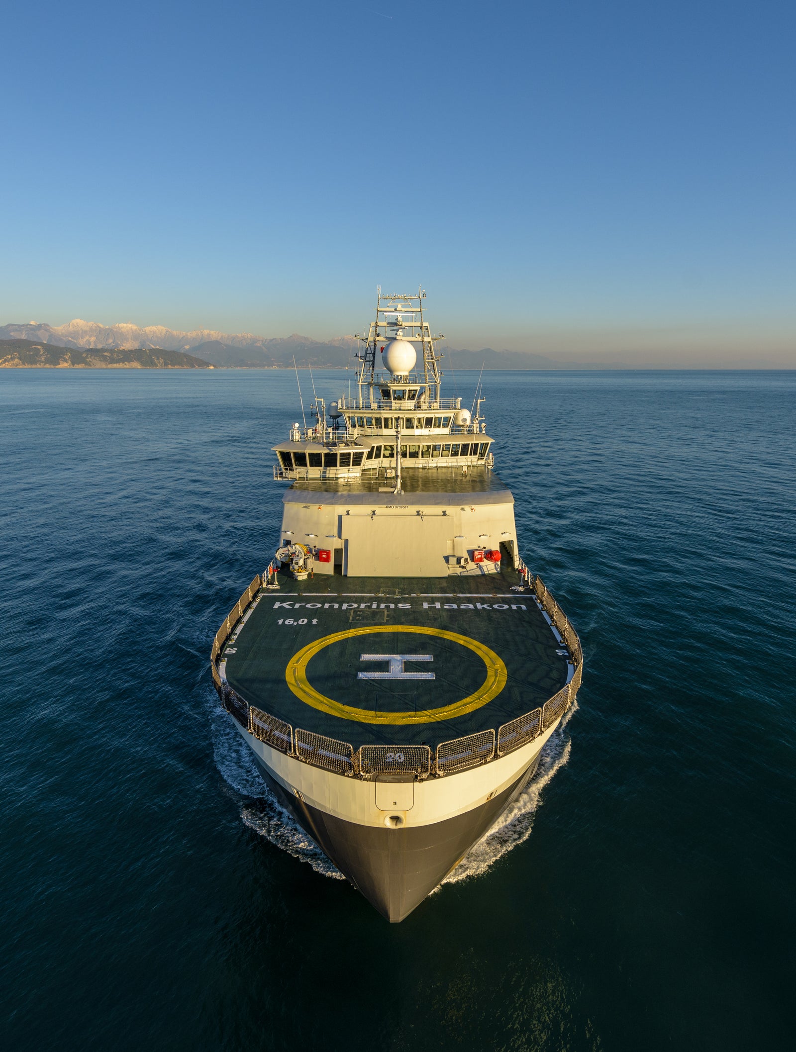 Prodotto - Nave da Ricerca Polare: Vista laterale della nave operativa in navigazione, elisuperficie sul ponte, struttura moderna ben visibile, sfondo marino con terre all’orizzonte.