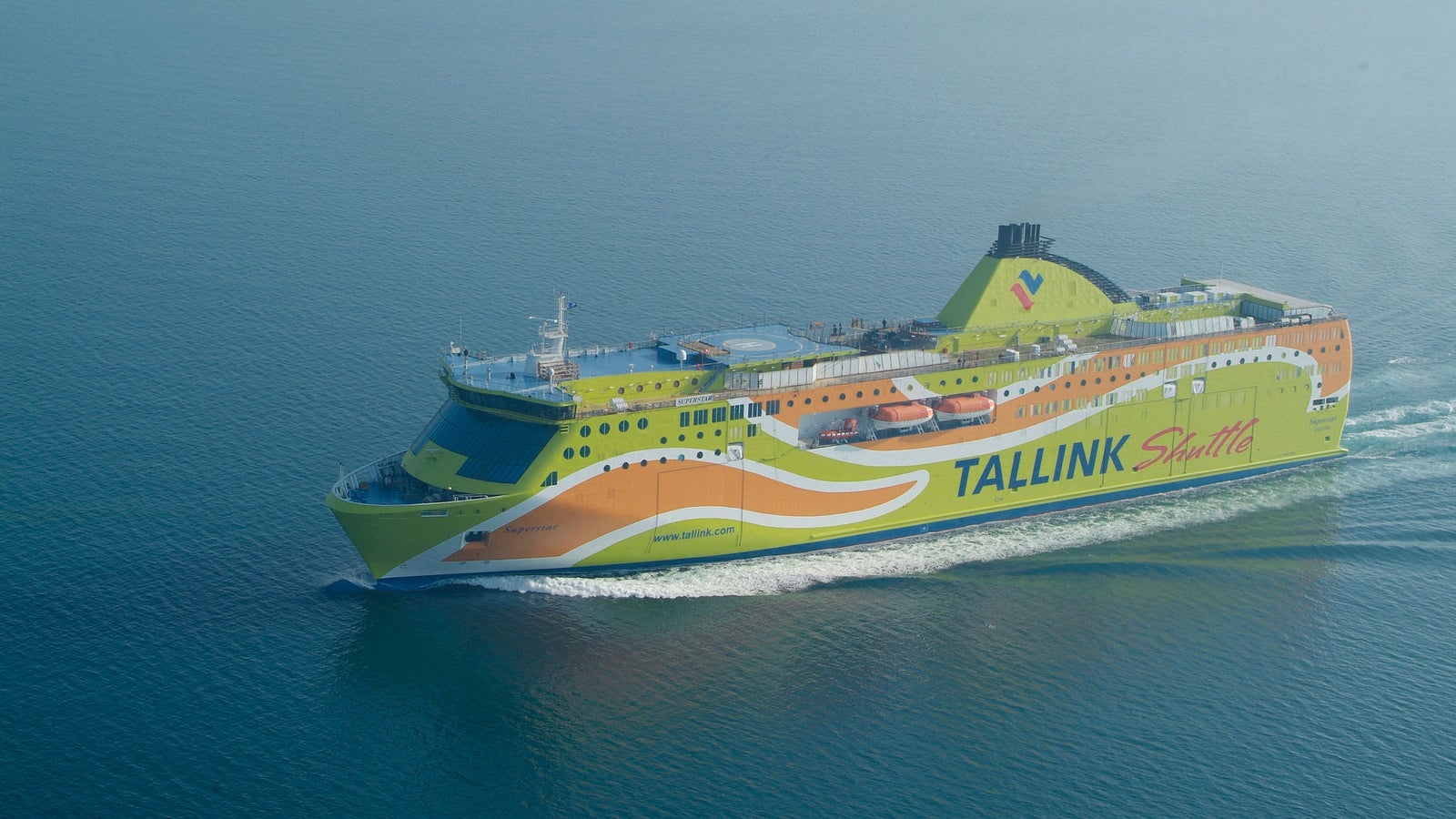 Fincantieri | Group - Business - Products - Ferries - Superstar: Vibrant Tallink Shuttle ferry in operation, green and yellow design, sleek structure, modern features, "Tallink Shuttle" text prominently visible on side, cruising across calm blue waters.