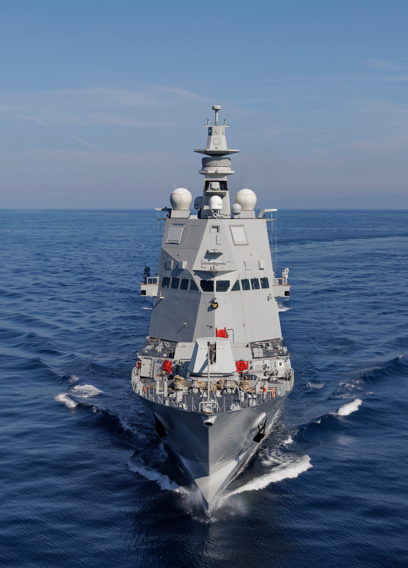 Fincantieri | Gruppo - Sostenibilità - Eccellenza industriale - Cilenti: Nave da guerra moderna operativa in navigazione su acque calme sotto cielo blu sereno, dotata di sistemi radar avanzati, antenne e design aerodinamico, dettagli rossi sul ponte e scafo grigio; focus su tecnologia e capacità marittime.