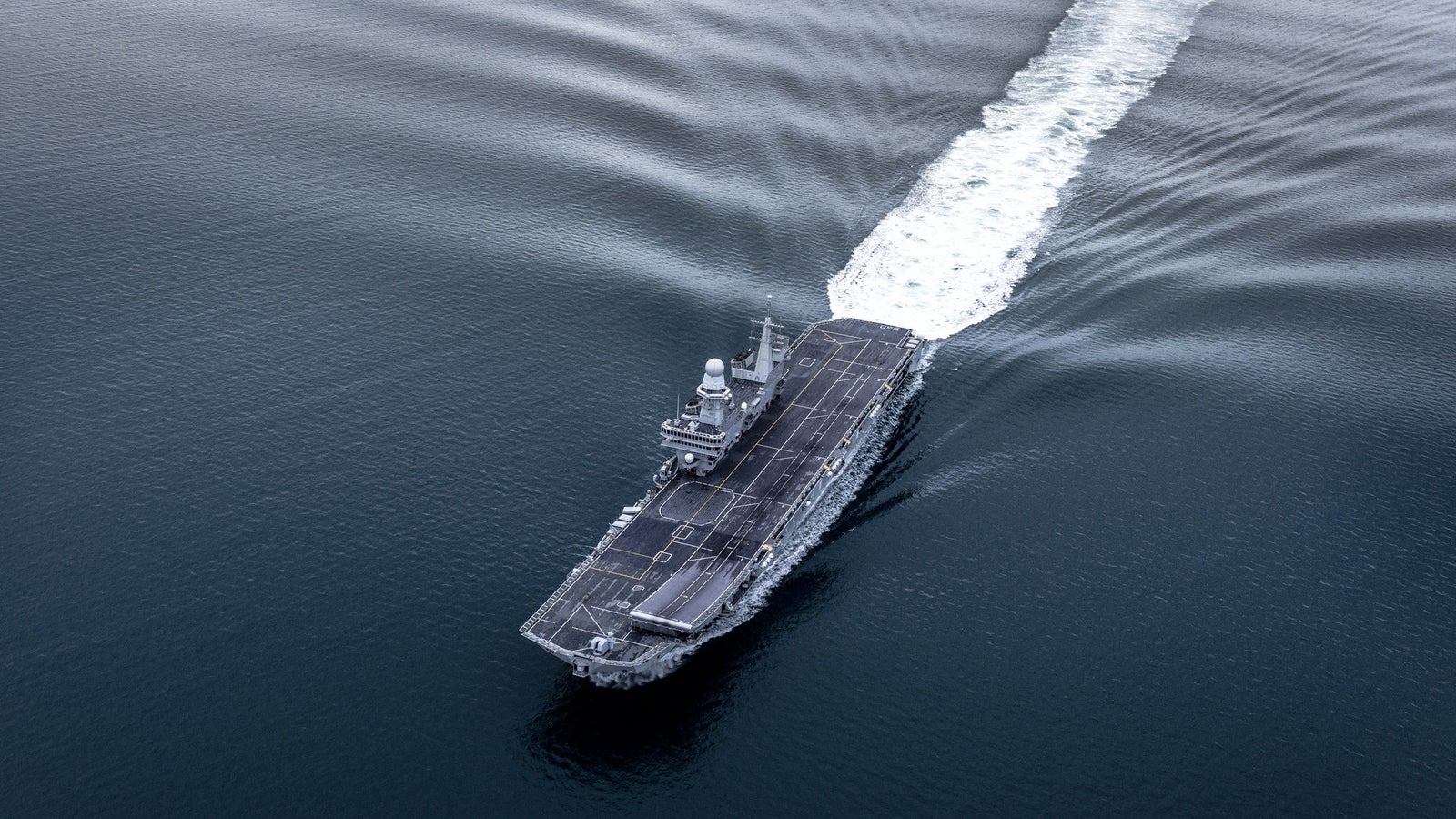 Fincantieri | Group - Business - Products - Naval Vessels - Aircraft Carriers and Amphibious Ships - Cavour: Aerial view of aircraft carrier "Cavour" in operation, visible flight deck, navigating open waters.