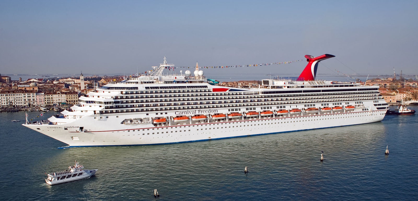 Fincantieri | Gruppo - Business - Prodotti - Navi da Crociera - Carnival Freedom: Nave da crociera Carnival Freedom ormeggiata vicino alla storica città di Venezia, esterno bianco con accenti rossi e blu, caratteristico fumaiolo rosso ben visibile.