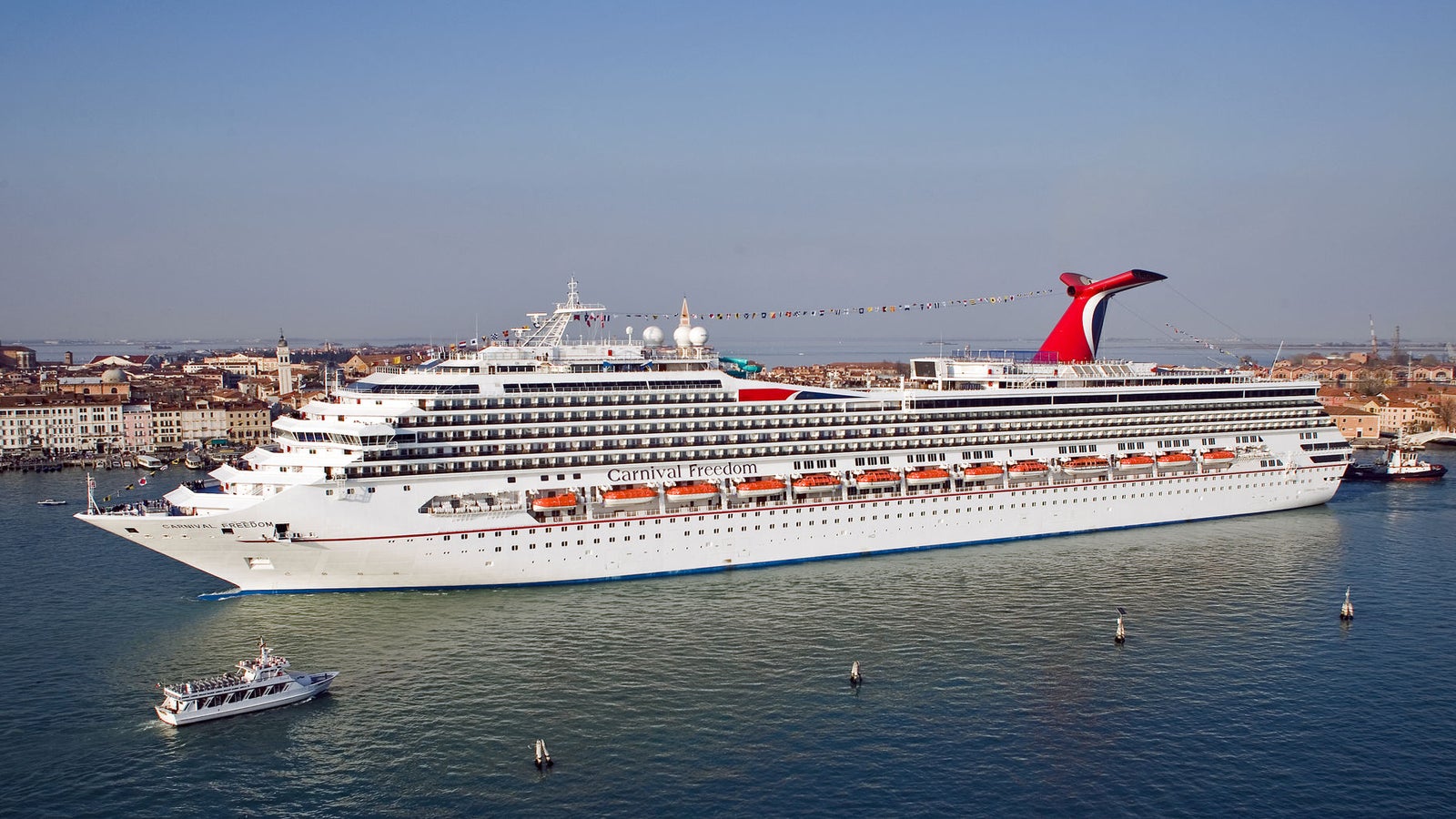 Fincantieri | Gruppo - Business - Prodotti - Navi da Crociera - Carnival Freedom: Nave da crociera Carnival Freedom ormeggiata vicino alla storica città di Venezia, esterno bianco con accenti rossi e blu, caratteristico fumaiolo rosso ben visibile.