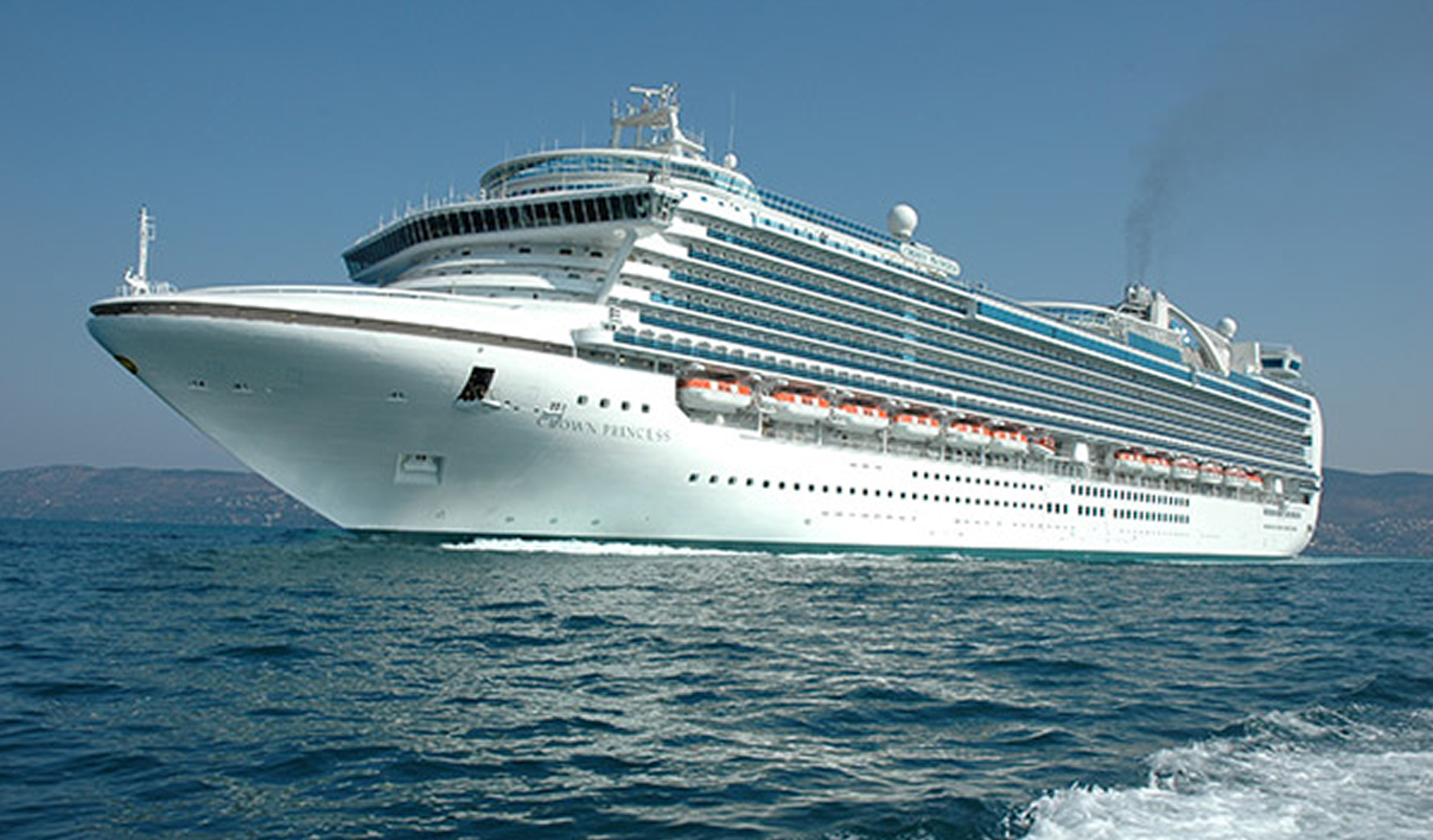 Fincantieri | About Us - Heritage and Future: Large white cruise ship 'Ocean Princess' operating on calm blue waters, multiple decks with visible lifeboats, sleek design and smoke from the funnel. Clear sky.