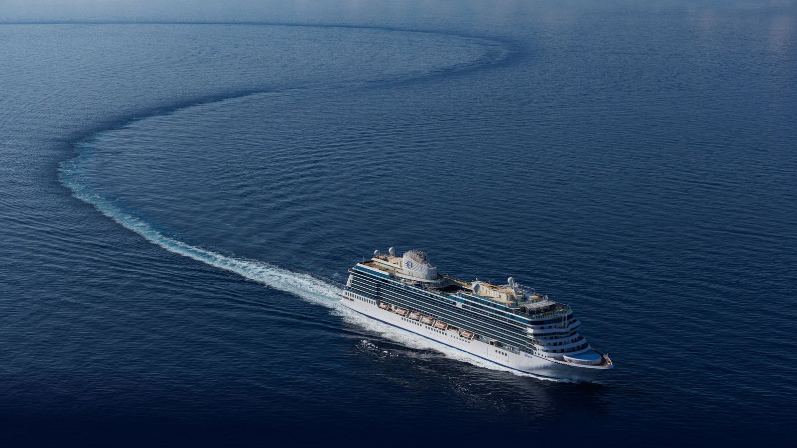 Fincantieri | Services - Naval After-Sales: Side view of a modern operational cruise ship sailing on calm waters, multiple decks and elegant design, visible wake, serene ocean environment.