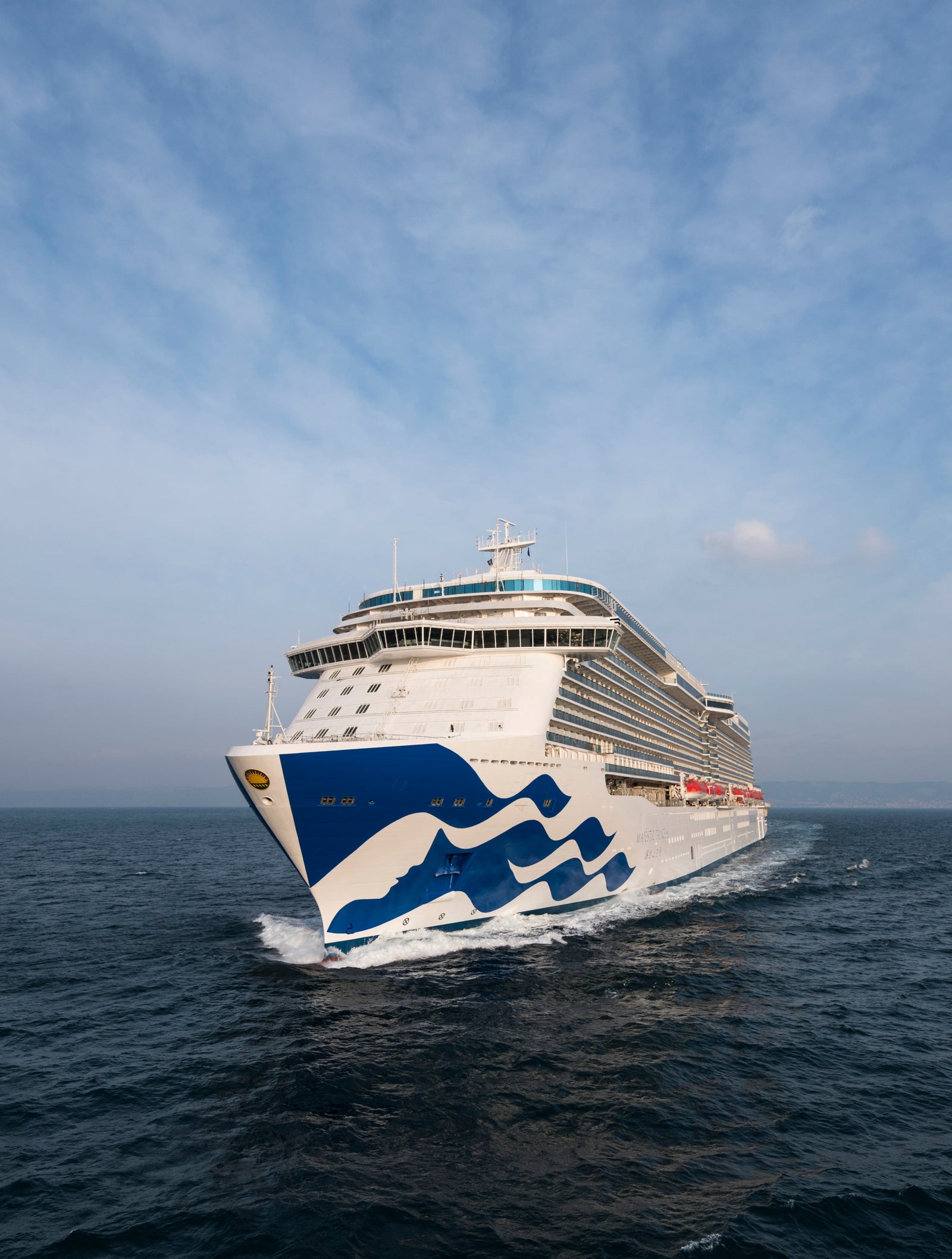 Fincantieri | Group - Business - Products - Cruise Ships - Majestic Princess: Large operational luxury cruise ship sailing on calm ocean waters under partly cloudy sky, blue wave design on hull and multiple decks with visible balconies.