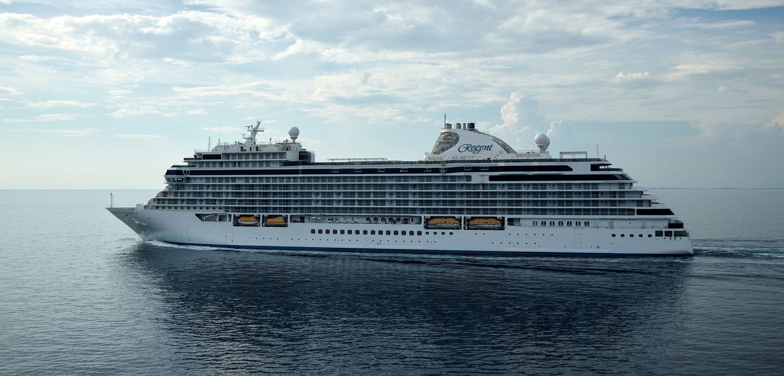 Fincantieri | Group - Business - Products - Cruise Ships - Seven Seas Splendor: Large modern luxury cruise ship in operation, sailing on calm waters under partly cloudy sky, multiple decks with balconies and visible lifeboats.