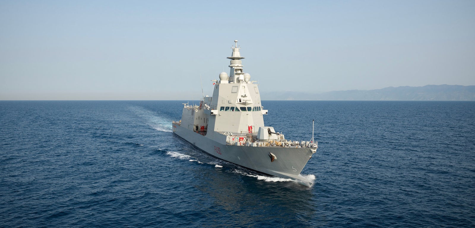  Fincantieri | Gruppo - Business - Prodotti - Navi per la difesa - Fregate - Classe Thaon de Revel: Vista laterale della nave operativa in navigazione, scafo grigio moderno, radar e antenne visibili, sfondo con sagome terrestri.