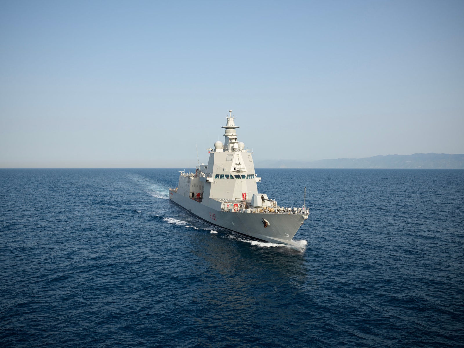 Fincantieri | About Us - Heritage and Future: Operational warship sailing on calm sea, aerial view with diagonal framing, side of the ship visible as it glides over the waves.