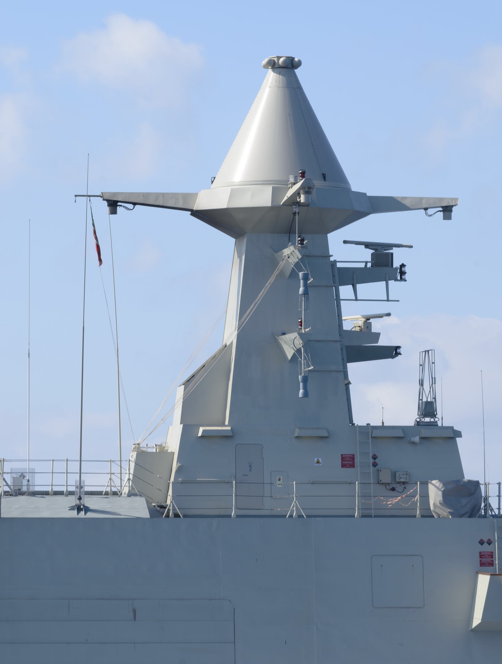 Fincantieri | Group - Business - Products - Defence Vessels - Corvettes - Abu Dhabi class: Close-up view of naval radar system mounted on warship, angular components and antennas visible, maritime environment and clear sky, advanced technology.