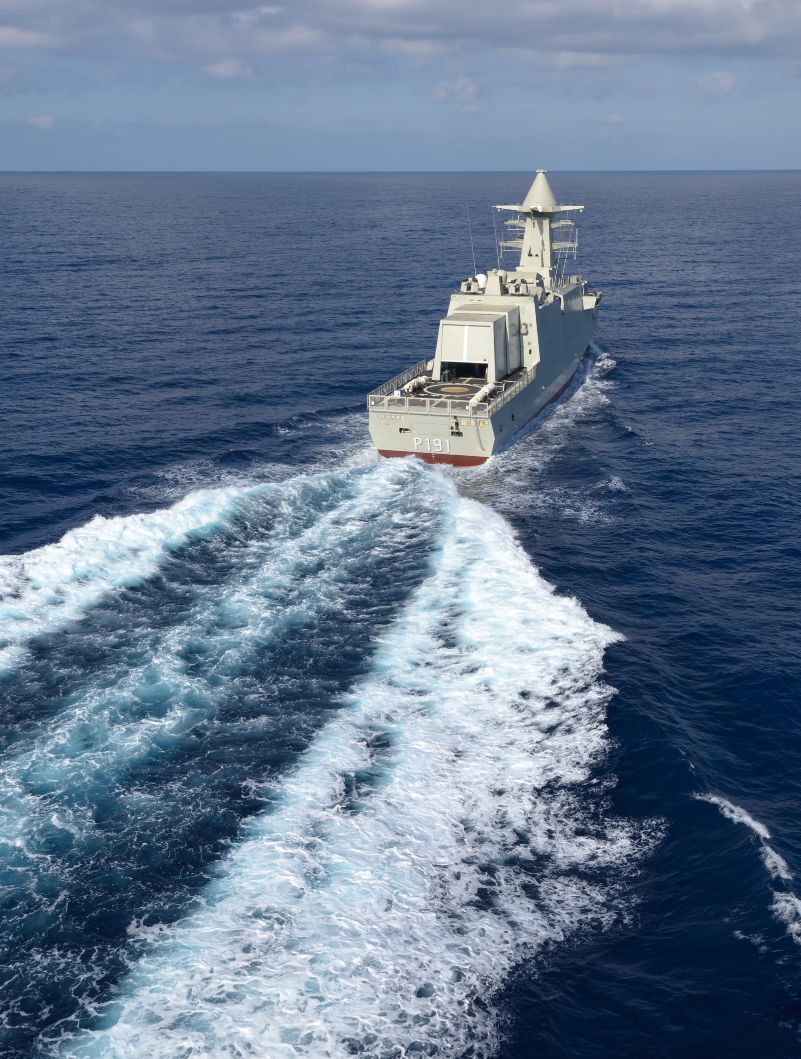 Fincantieri | Group - Business - Products - Defence Vessels - Corvettes - Abu Dhabi class: Modern naval ship in operation, structure and details clearly visible, sailing through open ocean, trail of white waves, deep blue water, partly cloudy sky.
