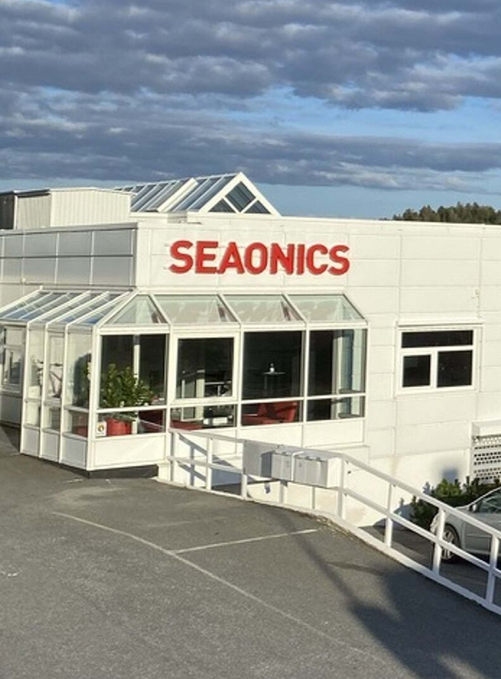 Fincantieri | Group - Subsidiaries and Affiliates - Vard Seaonics: Seaonics company building, modern white structure with large glass windows; mountain and cloudy sky backdrop, 'Seaonics' clearly displayed on facade.
