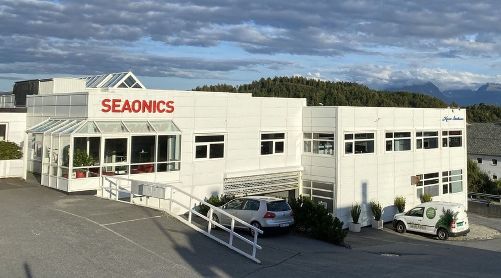 Fincantieri | Group - Subsidiaries and Affiliates - Vard Seaonics: Seaonics company building, modern white structure with large glass windows; mountain and cloudy sky backdrop, 'Seaonics' clearly displayed on facade.