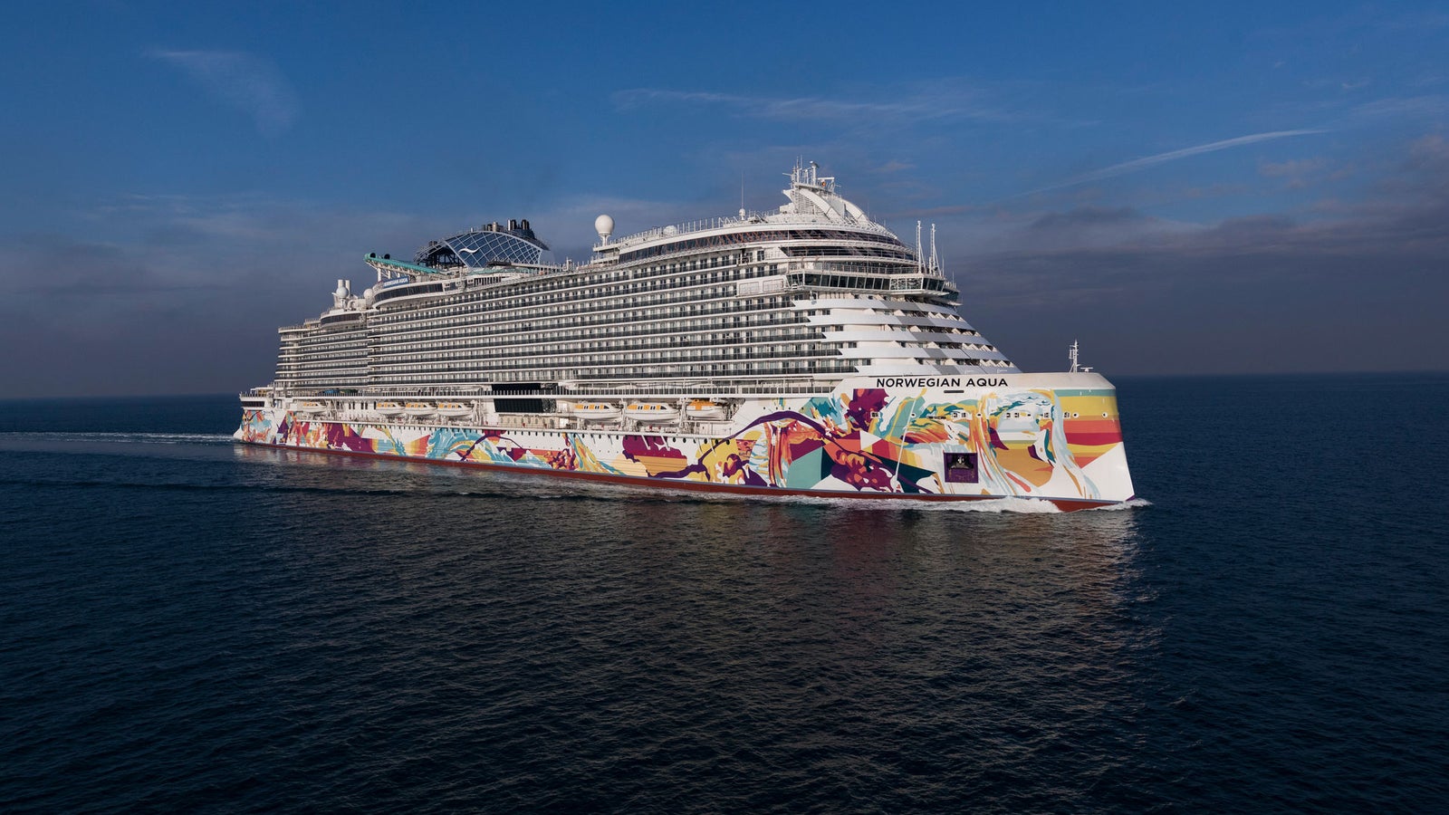  Fincantieri | Gruppo - Business - Prodotti - Navi da Crociera - Norwegian Aqua: Modern cruise ship with intricate blue and white design in operation, navigating calm waters under cloudy sky, multiple decks with outdoor recreation areas, name 'Norwegian Viva' visible on bow.