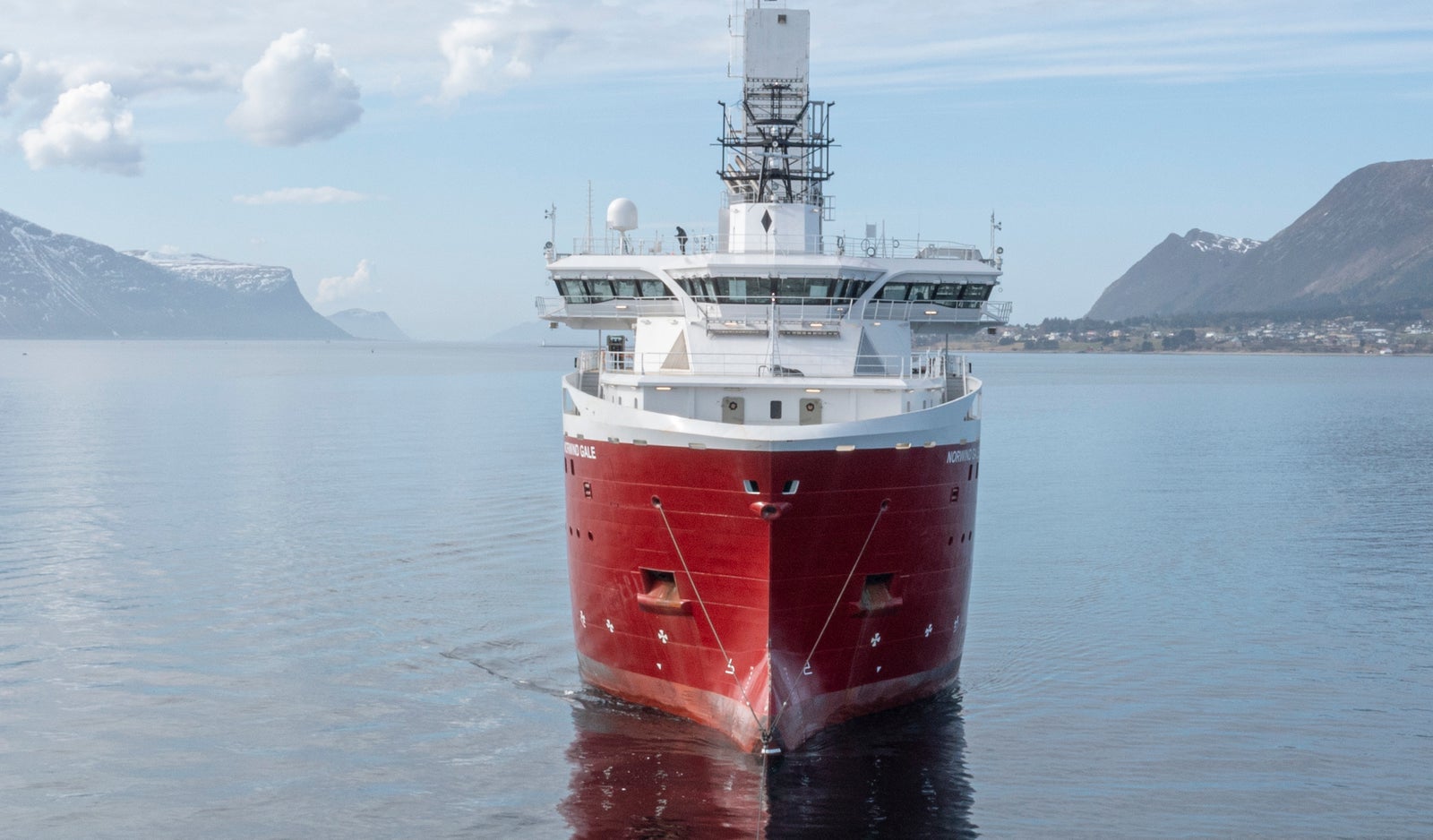 Fincantieri | Prodotti - Servizi - Riparazione e trasformazioni navali - Nave moderna: Nave rossa operativa al centro delle acque, design marittimo moderno con torre prominente, sfondo paesaggio nordico con montagne e nuvole.