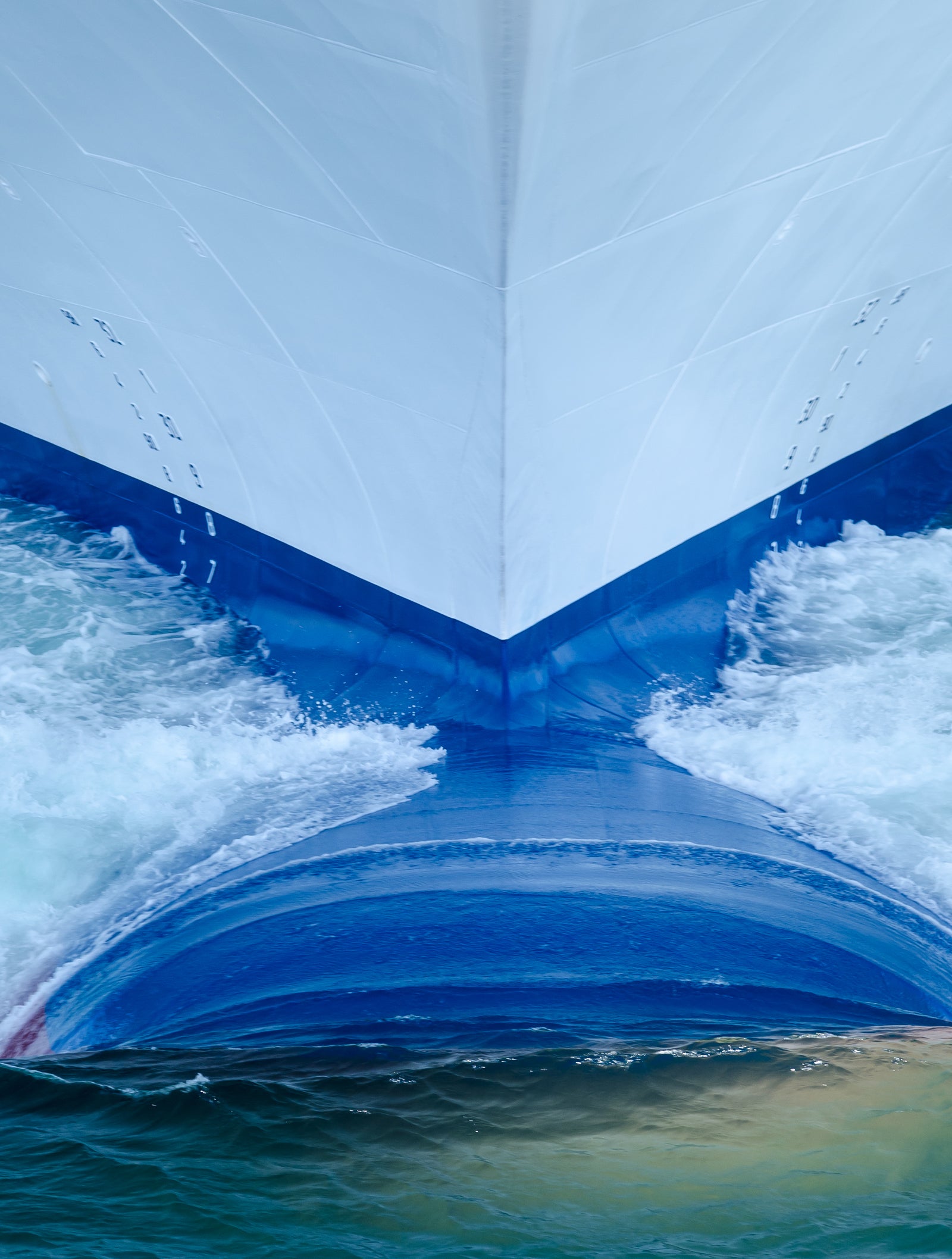 Fincantieri | Group - Business - Products - Cruise Ships - Carnival Breeze: Close-up of Carnival Breeze cruise ship bow in operation cutting through ocean, dynamic waves and foam, modern design with vivid blue accents, captures energy and movement of maritime travel, light reflections on water surface.