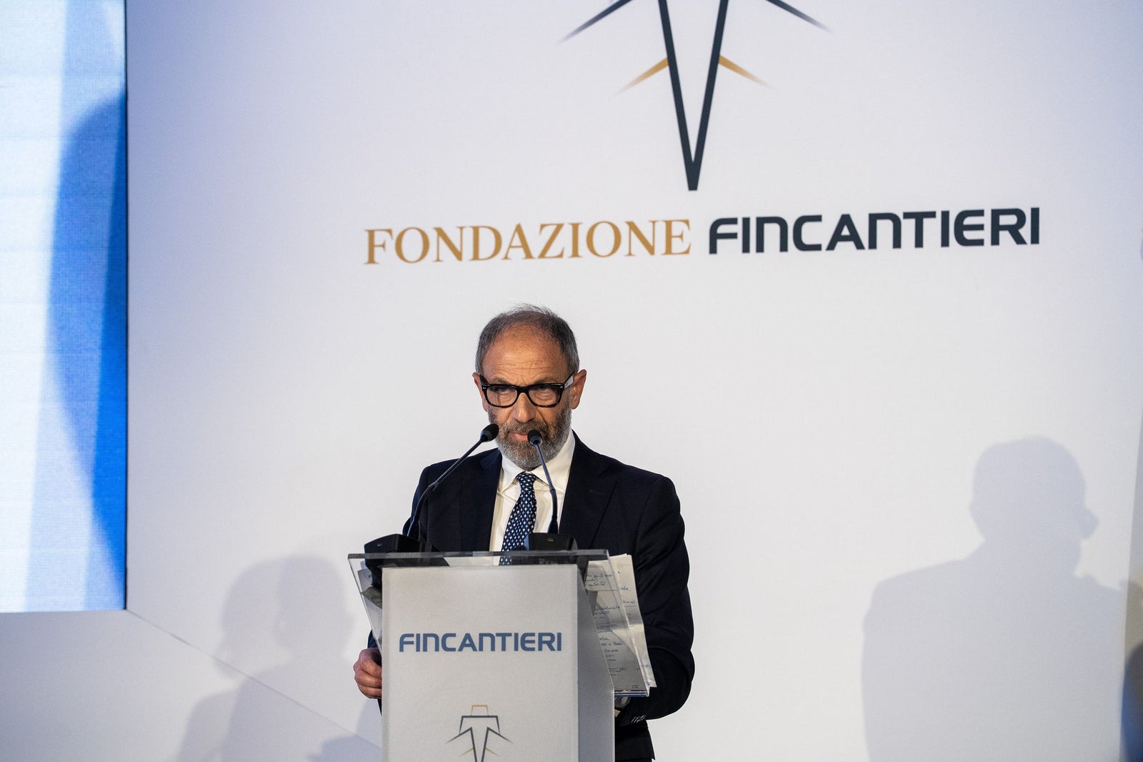 Newsroom - Comunicati stampa - 2025 - Gruppo Fincantieri: Un anno di Fondazione Fincantieri: storia, innovazione e impatto sociale: Primo piano di un relatore al podio con il logo Fondazione Fincantieri, durante evento istituzionale, sfondo chiaro e documenti in mano.