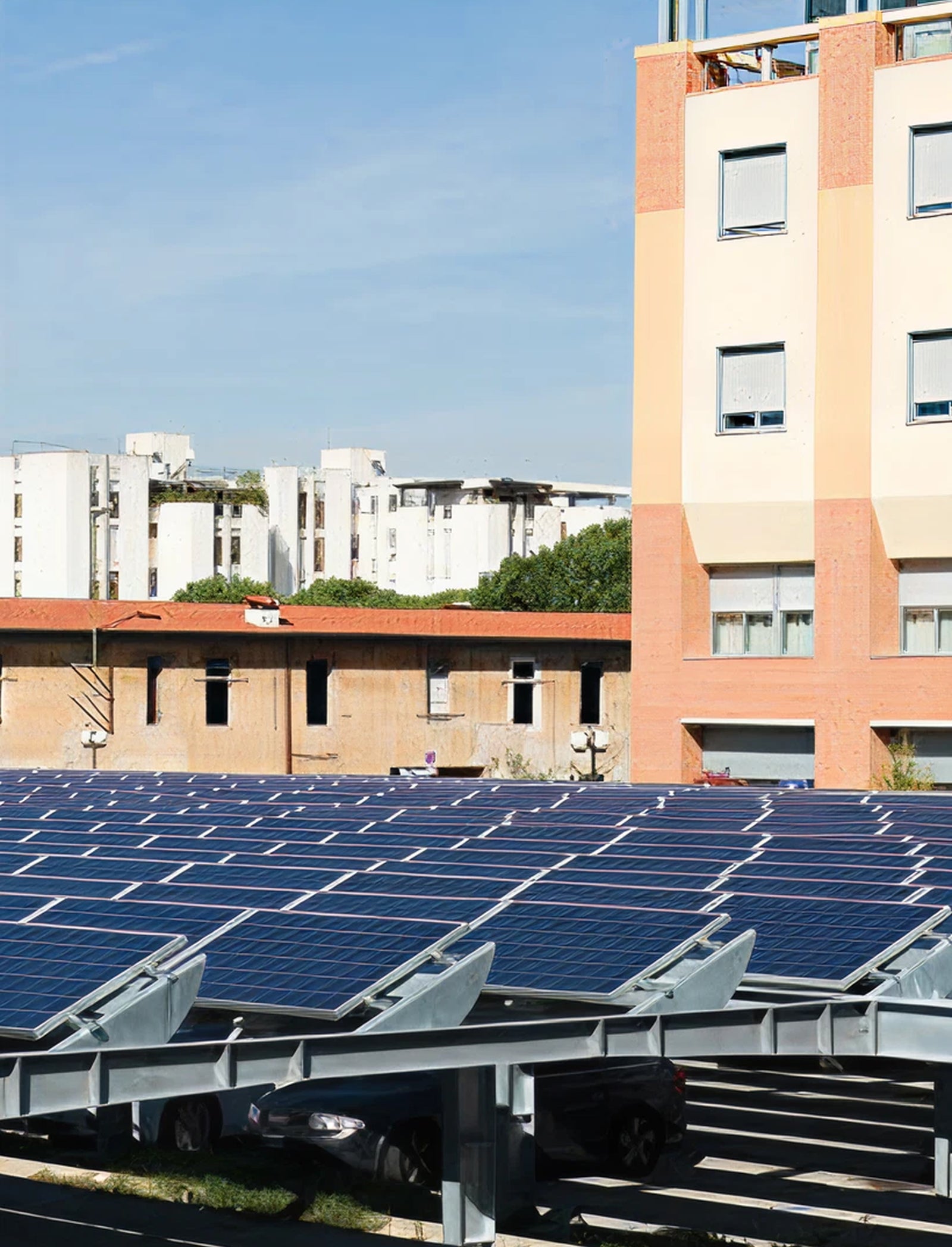 Fincantieri | Group - Subsidiaries and Affiliates - SOF: Field of solar panels installed in urban environment near residential buildings with modern architecture, panels arranged in rows capturing sunlight under clear blue sky; scene highlights sustainable energy solutions integrated into cityscapes.
