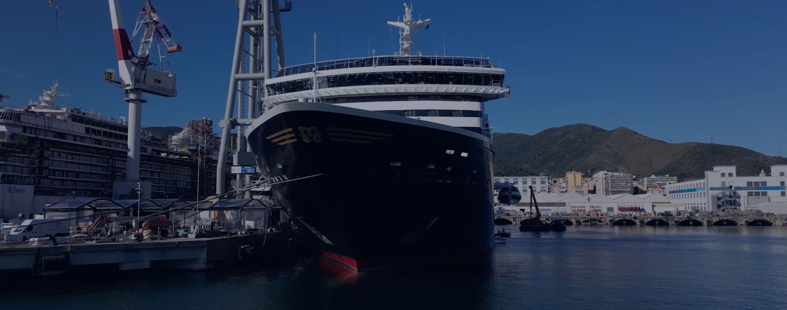 Fincantieri | Group - Business - Products - Integrated Electrical, Electronic and Electromechanical Systems - Ship maintenance: Close-up view of ship docked during maintenance operations, structural details evident, port environment.