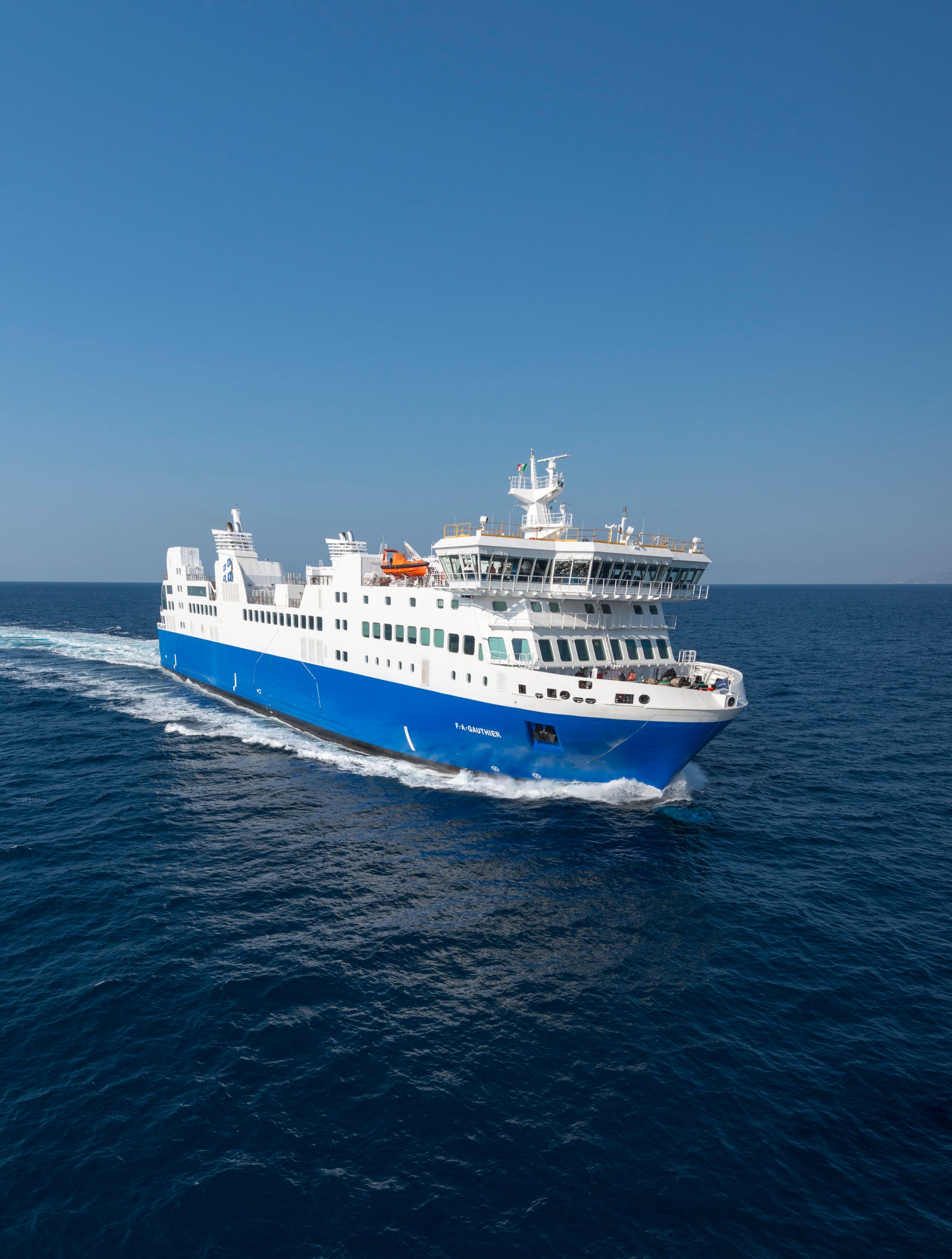 Fincantieri | Group - Business - Products - Ferries - Cruise FA Gauthier: Large blue and white "FA Gauthier" ferry in operation, multiple decks, visible lifeboats, cruising through deep blue waters, clear sky.