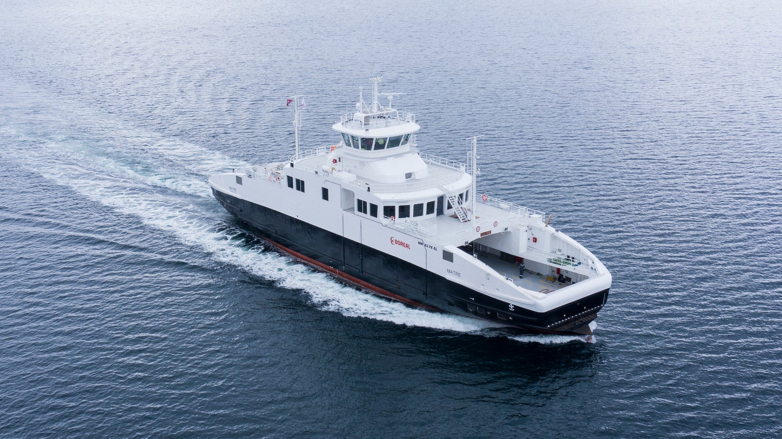 Fincantieri | Group - Business - Products - Ferries - Matre: White Matre ferry in operation, creating gentle ripples, navigating blue waters, distant snow-capped mountains, overcast sky.