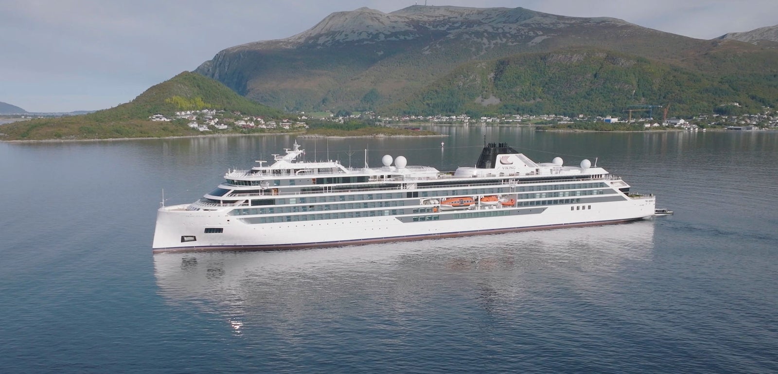 Fincantieri | Group - Business - Products - Cruise Ships - Viking Polaris: Side view of Viking Polaris cruise ship in operation in fjord, modern white hull, multiple decks, hilly and mountainous background.