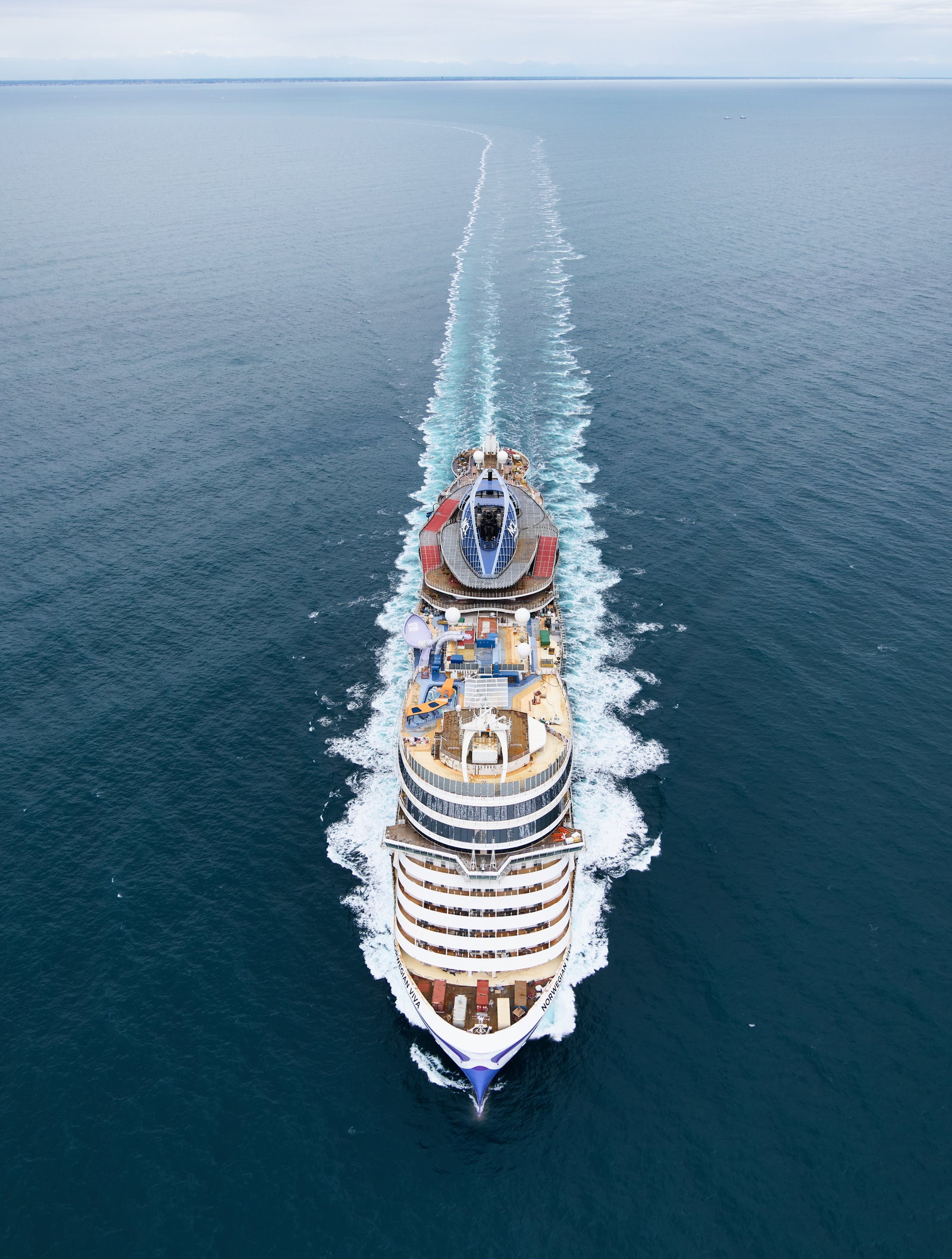 Fincantieri | Gruppo - Business - Prodotti - Navi da Crociera - Norwegian Viva: Grande nave da crociera operativa in navigazione su acque oceaniche calme e aperte, scia visibile, più ponti e aree ricreative, senza loghi o scritte, cielo coperto e ampio orizzonte blu.