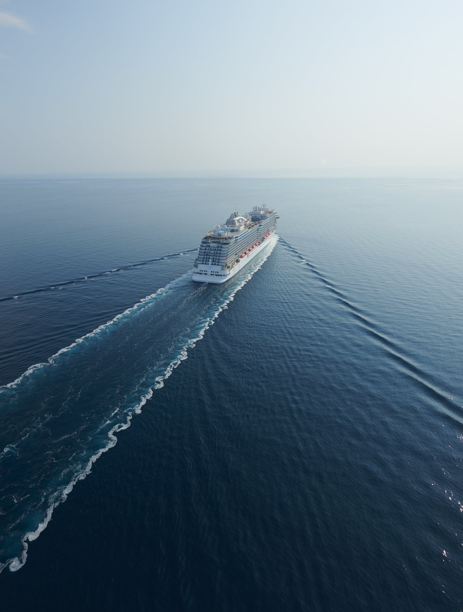 Fincantieri | Gruppo - Business - Prodotti - Navi da Crociera - Sky Princess: Grande nave da crociera di lusso operativa identificata come 'Sky Princess', naviga su oceano aperto sotto cielo parzialmente nuvoloso, più ponti, scialuppe di salvataggio visibili, design architettonico moderno, scia con pattern dinamici che enfatizza movimento e scala.