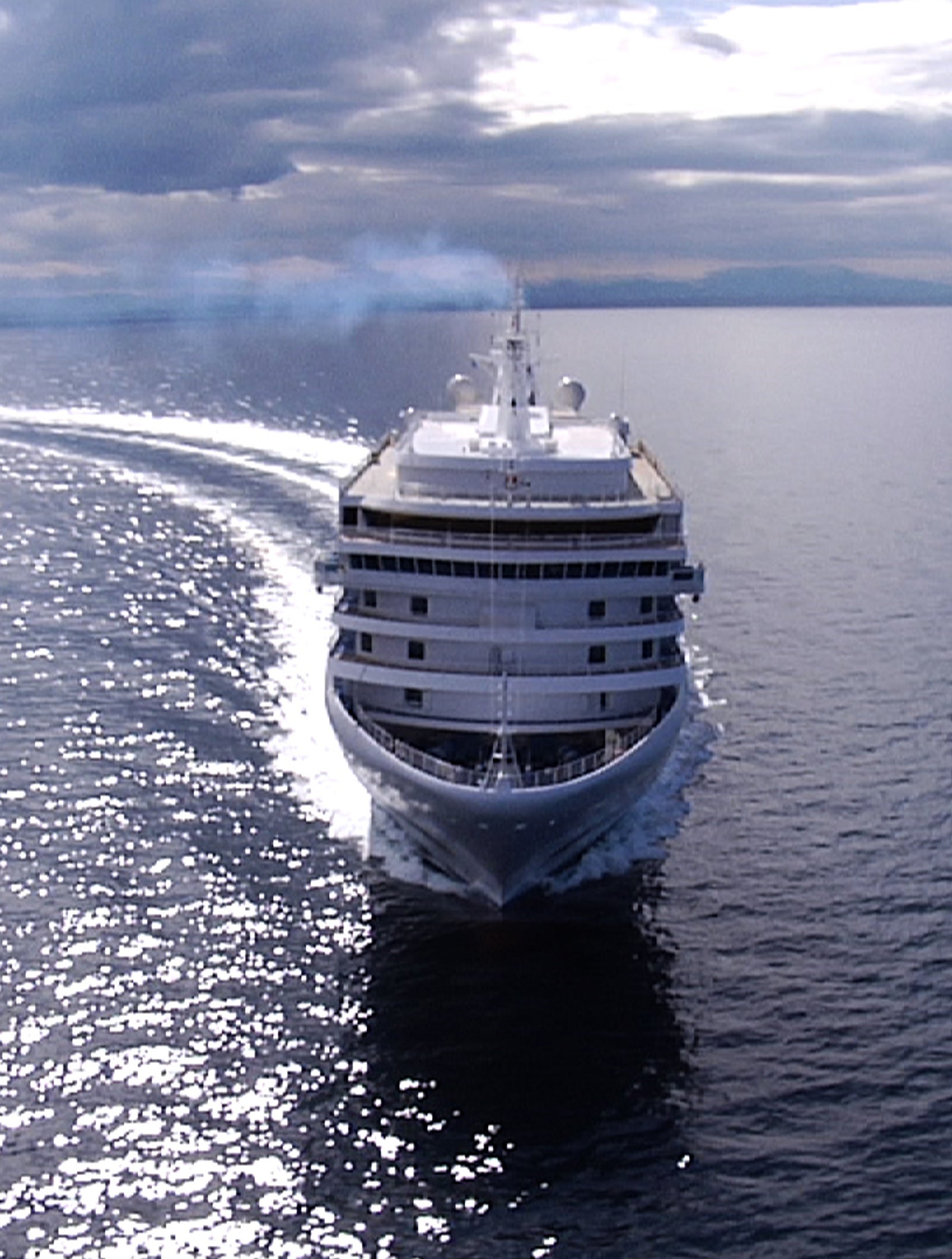 Fincantieri | Group - Business - Products - Cruise Ships - Silver Spirit: Large modern operational cruise ship sailing on calm waters under cloudy sky, visible wake, multiple decks with balconies and elegant details, setting conveys relaxation and luxury associated with maritime travel.