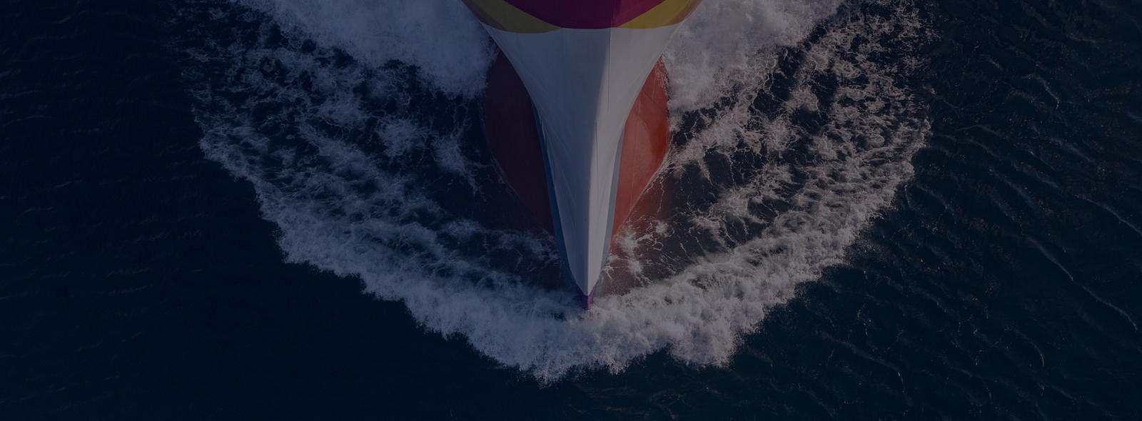 Fincantieri | Group - Innovation - Smart Manufacturing System: Brightly colored boat in red, yellow, and white seen from above while crossing deep blue ocean waters, foamy waves generated by its movement, image highlighting the dynamism and aesthetics of sea travel.