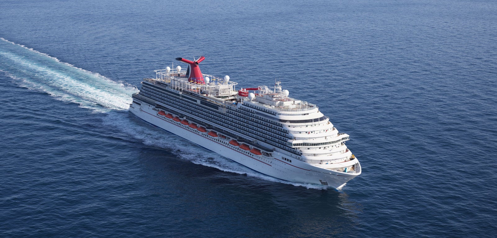 Fincantieri | Gruppo - Business - Prodotti - Navi da Crociera - Carnival Panorama: Nave da crociera imponente operativa che scivola su oceano calmo e aperto sotto cielo limpido, più ponti, accenti rossi e bianchi, camino distintivo, scia visibile che evidenzia movimento e velocità, scena che evoca avventura e relax sul mare.
