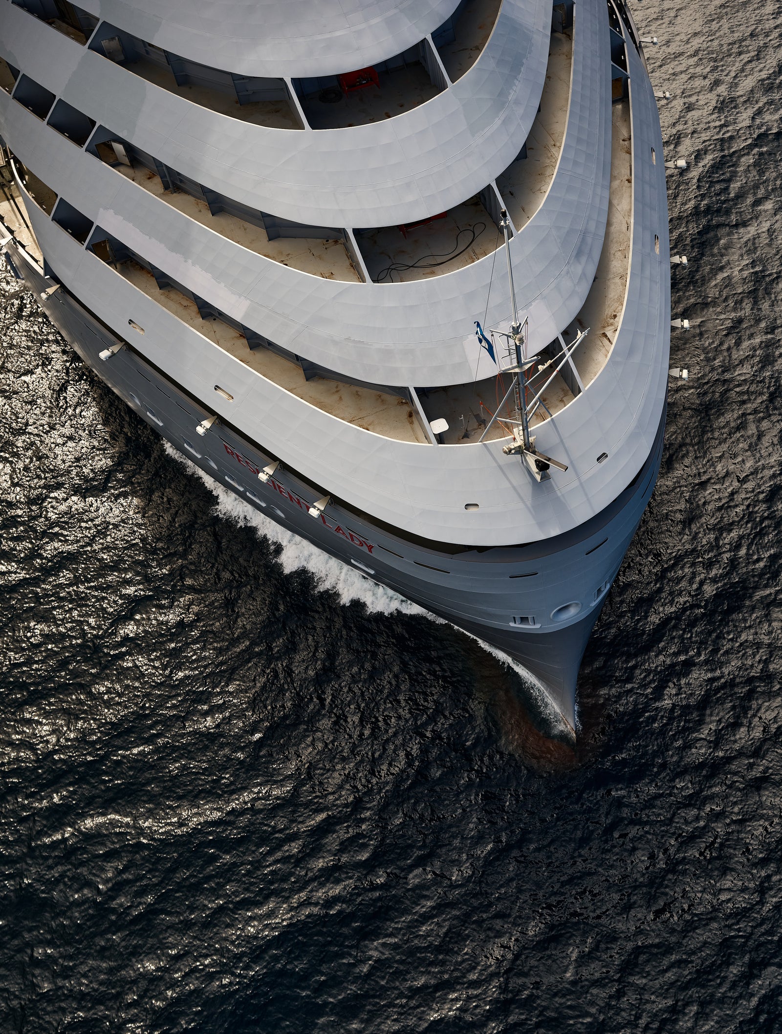 Fincantieri | Group - Business - Products - Cruise Ships - Resilient Lady: Modern operational cruise ship with elegant design and red details, name 'Resilient Lady' and Virgin Voyages branding clearly visible on hull, multiple decks and relaxation areas, sailing in calm waters under partly cloudy sky, atmosphere of luxury and adventure.