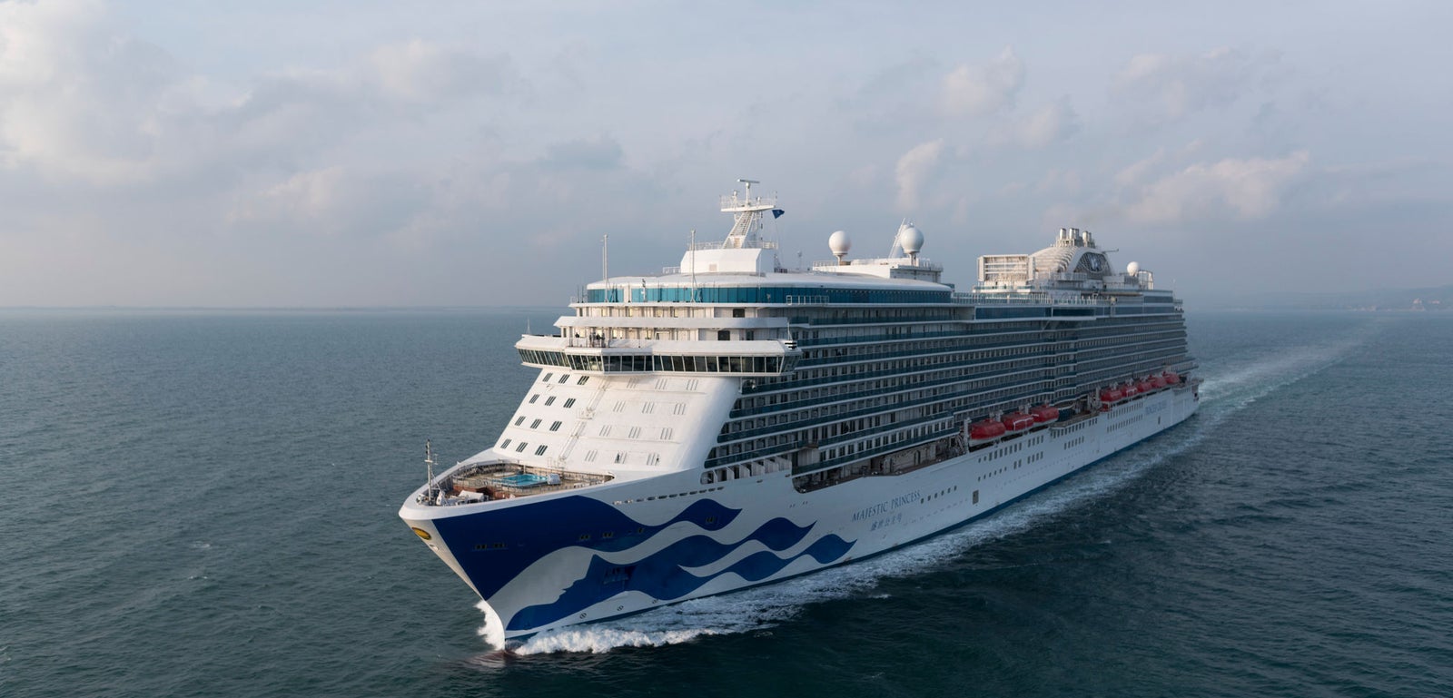 Fincantieri | Group - Business - Products - Cruise Ships - Majestic Princess: Large operational luxury cruise ship sailing on calm ocean waters under partly cloudy sky, wave design on hull and multiple decks with visible amenities.