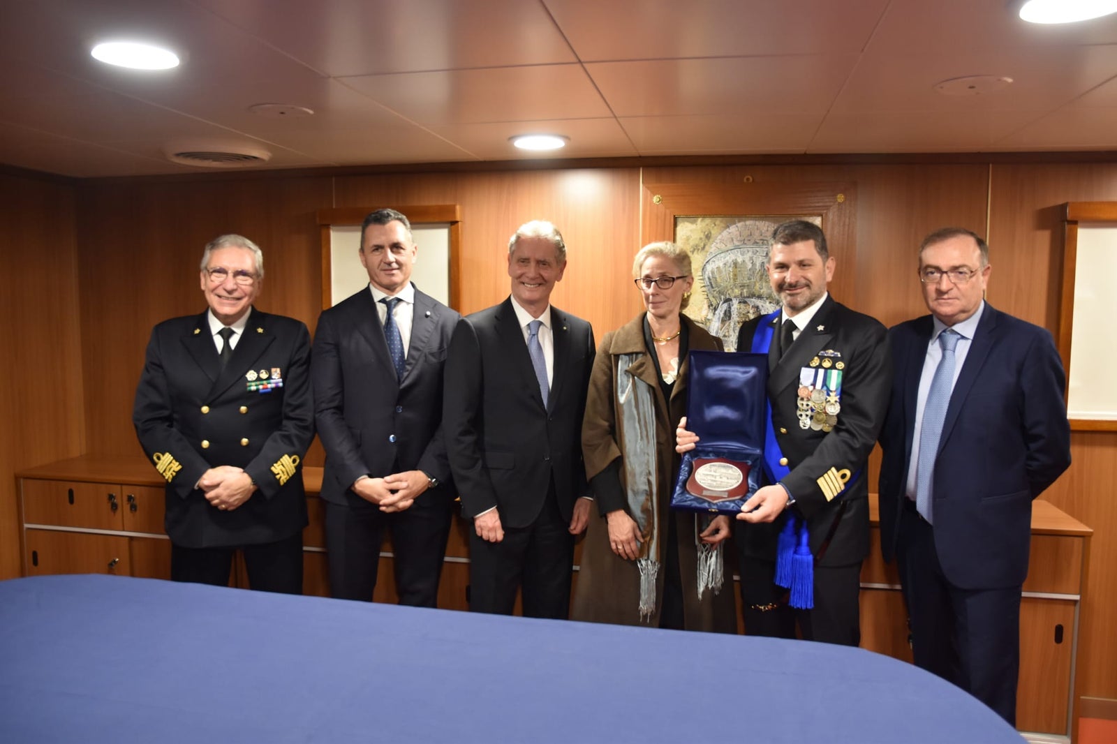 newsroom - press releases - 2025 - fincantieri group: fincantieri delivers "atlante", second lss unit for the italian navy: officers and representatives on board during the official handover, group photo with commemorative plaque in wood-panelled room.