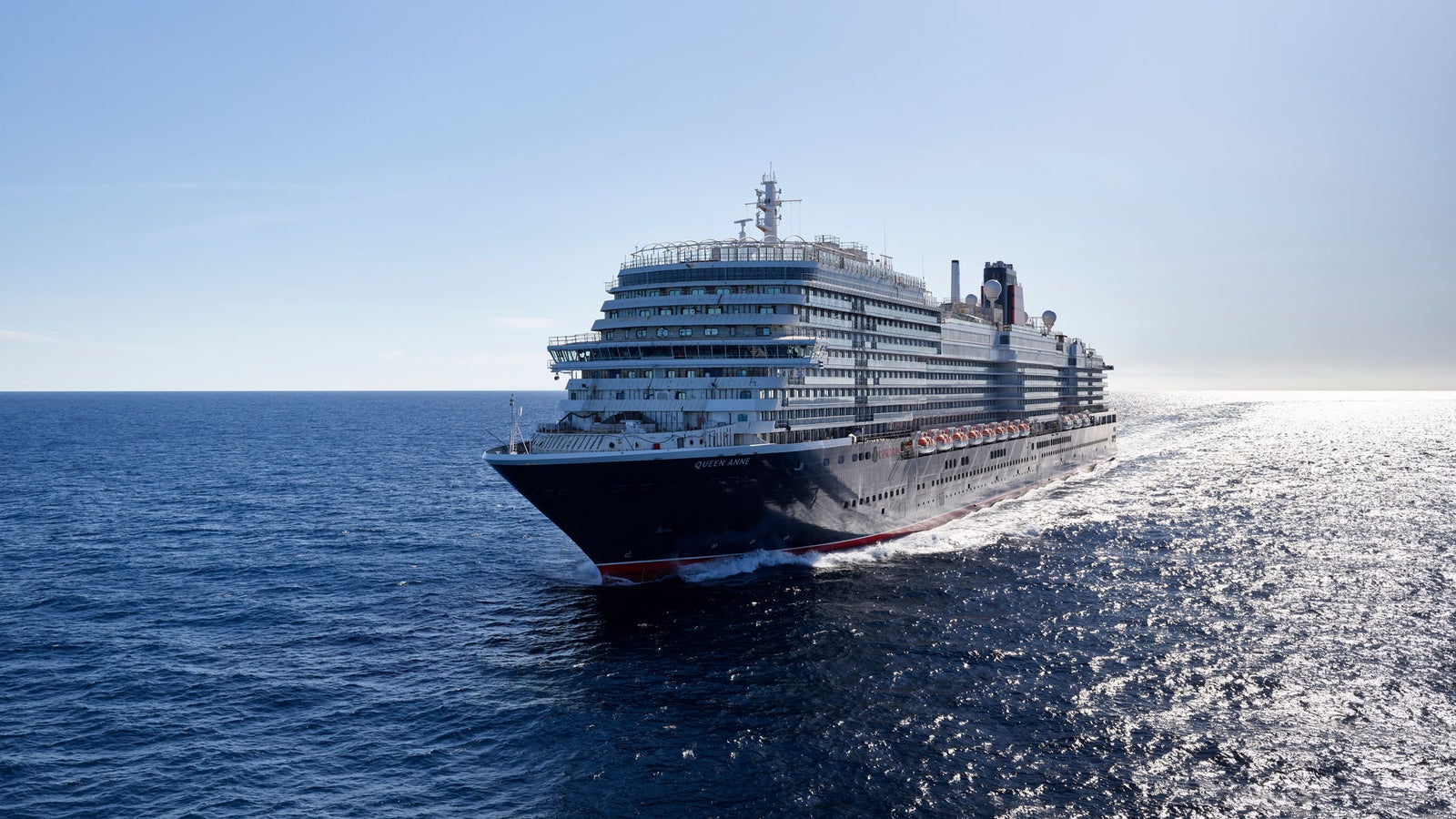 Fincantieri | Group - Business - Products - Cruise Ships - Queen Anne: Side view of Queen Anne cruise ship in operation, navigating open sea, light hull with linear profile, multiple passenger decks, name 'Queen Anne' visible on hull.