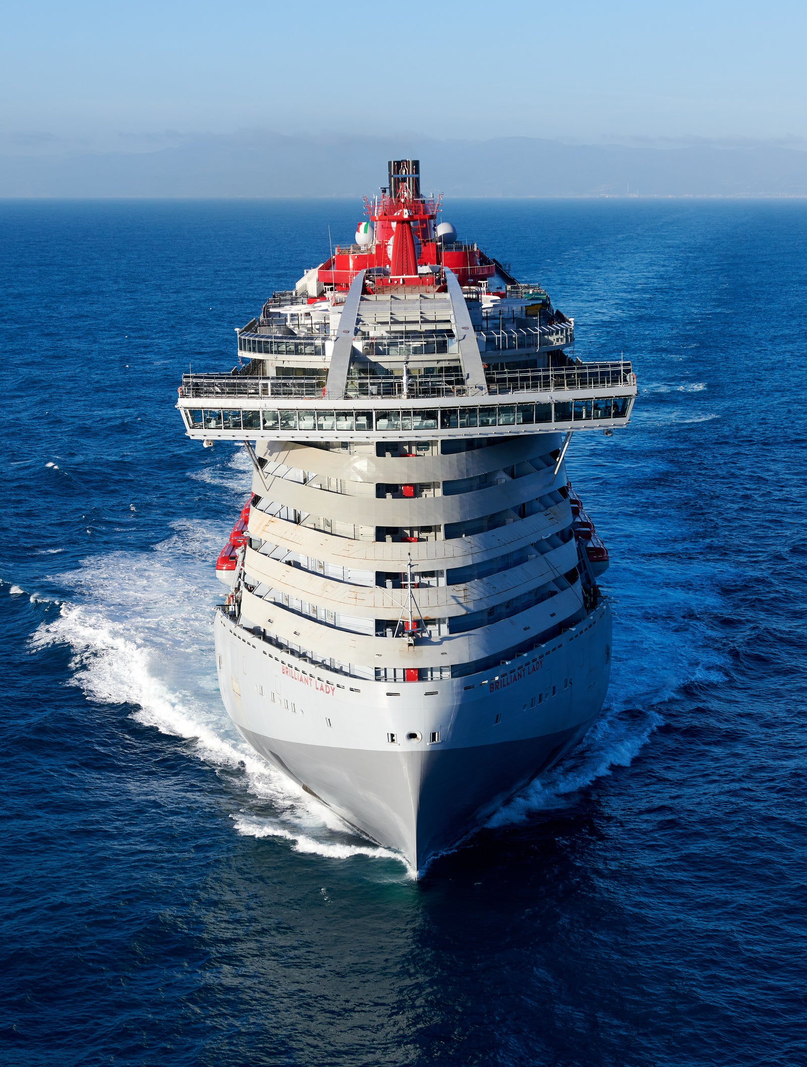 Fincantieri | Group - Business - Products - Cruise Ships - Brilliant Lady: Large modern operational cruise ship with elegant design and red details, multiple decks, name 'Brilliant Lady' visible on hull, sailing in calm waters under partly cloudy sky.