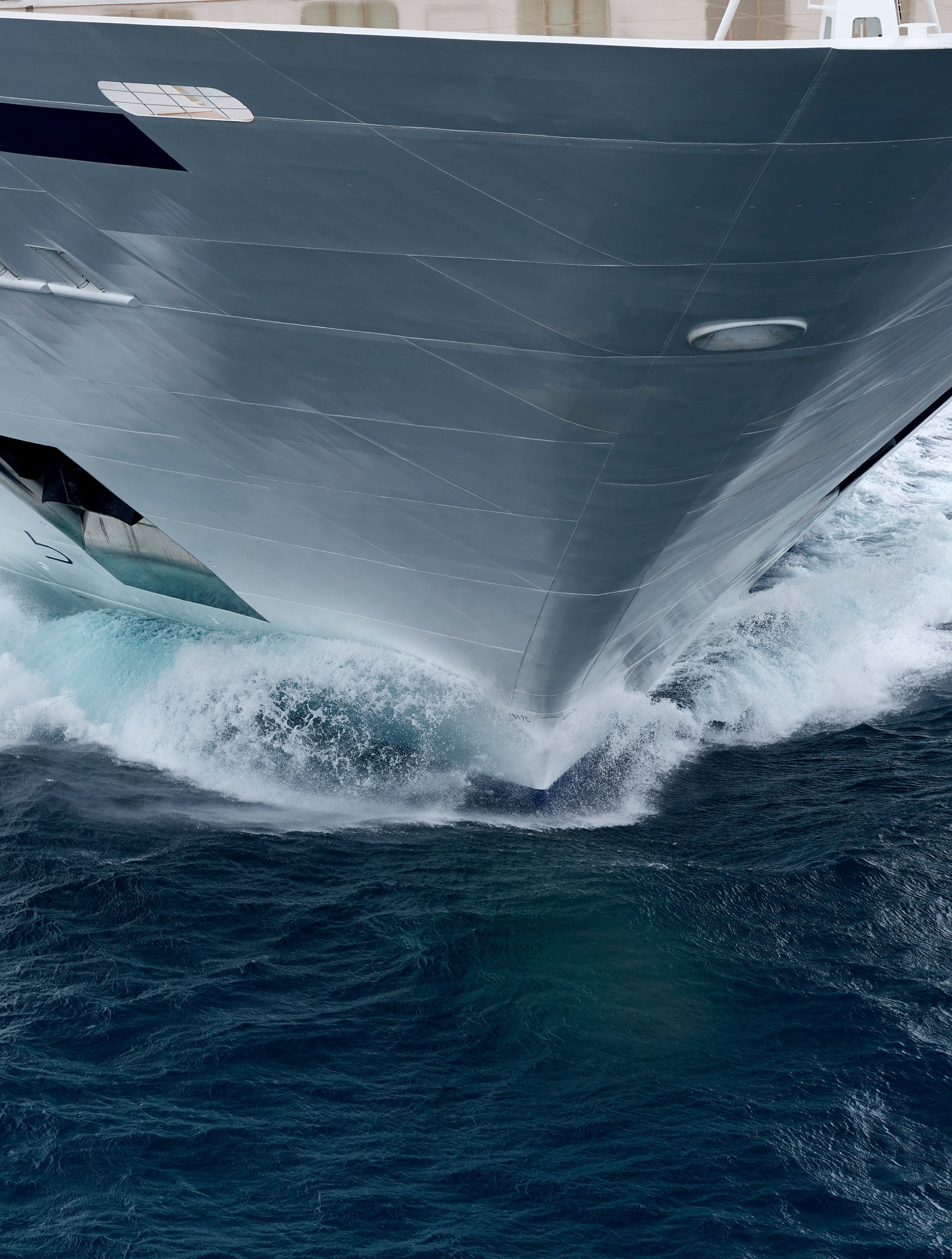 Fincantieri | Group - Business - Products - Cruise Ships - Viking Mars: Bow of large ship in operation slicing through ocean, dynamic white waves, sleek metallic design contrasting with deep blue water, power and motion in serene sea setting.