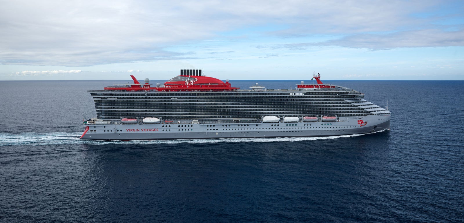 incantieri | Gruppo - Business - Prodotti - Navi da Crociera - Resilient Lady: Grande nave da crociera Virgin Voyages operativa con design moderno e dettagli rossi evidenti, più ponti, nome 'Resilient Lady' chiaramente visibile sullo scafo, camino rosso distintivo, naviga su acque calme sotto cielo parzialmente nuvoloso, atmosfera di lusso e avventura marittima.