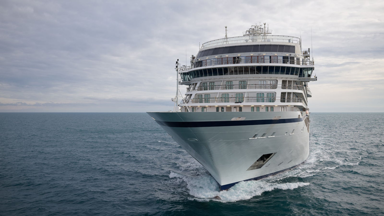 Fincantieri | Gruppo - Business - Prodotti - Navi da Crociera - Viking Mars: Vista di prua della nave Viking Mars operativa in navigazione su mare aperto, scafo bianco ben illuminato, più ponti con balconi e vetrate visibili, ampio cielo nuvoloso sopra l’orizzonte.