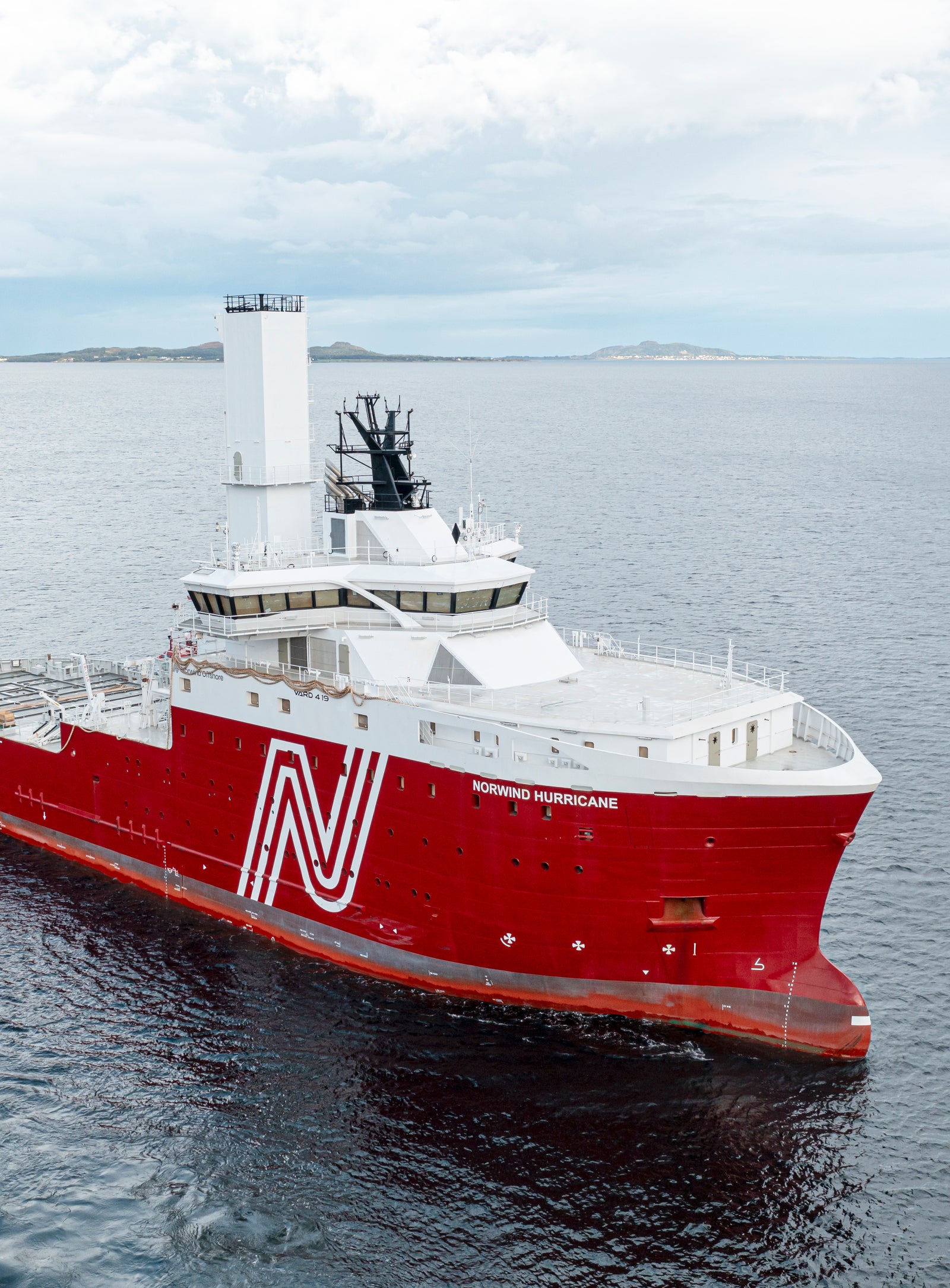 Fincantieri | Group - Subsidiaries and Affiliates - VARD: Striking red offshore vessel cruising in open waters under partly cloudy sky, prominent white 'N' logo on side, modern design elements including tall central tower; calm ocean and distant horizon create serene maritime setting.