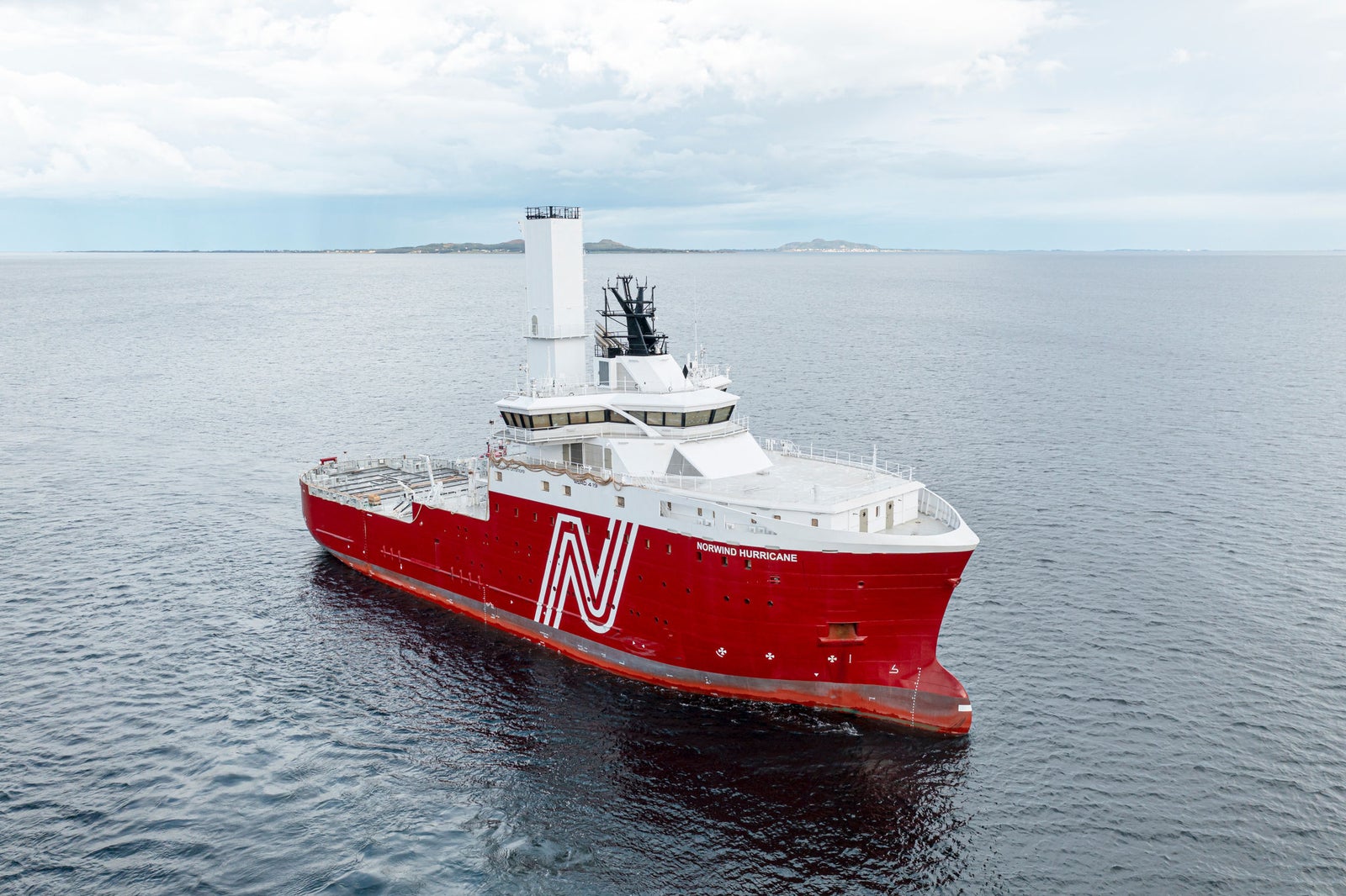 Fincantieri | Group - Subsidiaries and Affiliates - VARD: Striking red offshore vessel cruising in open waters under partly cloudy sky, prominent white 'N' logo on side, modern design elements including tall central tower; calm ocean and distant horizon create serene maritime setting.