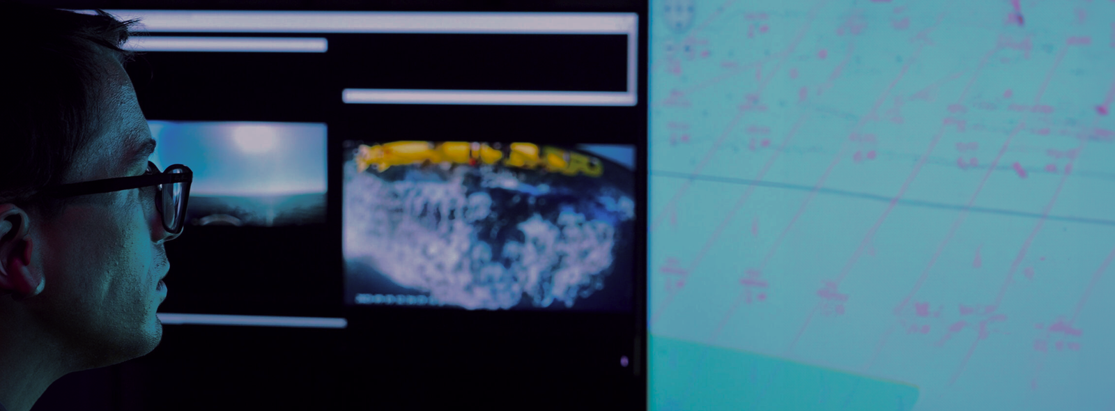 Fincantieri | Group - Business - Products - Critical Infrastructures - Digital monitoring workspace: Workspace with multiple digital screens displaying data, map coordinates, Earth and underwater visuals; high-tech environment focused on analysis or monitoring activities.