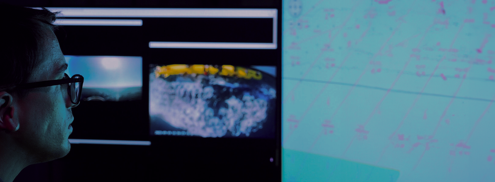 Fincantieri | Group - Business - Products - Critical Infrastructures - Digital monitoring workspace: Workspace with multiple digital screens displaying data, map coordinates, Earth and underwater visuals; high-tech environment focused on analysis or monitoring activities.