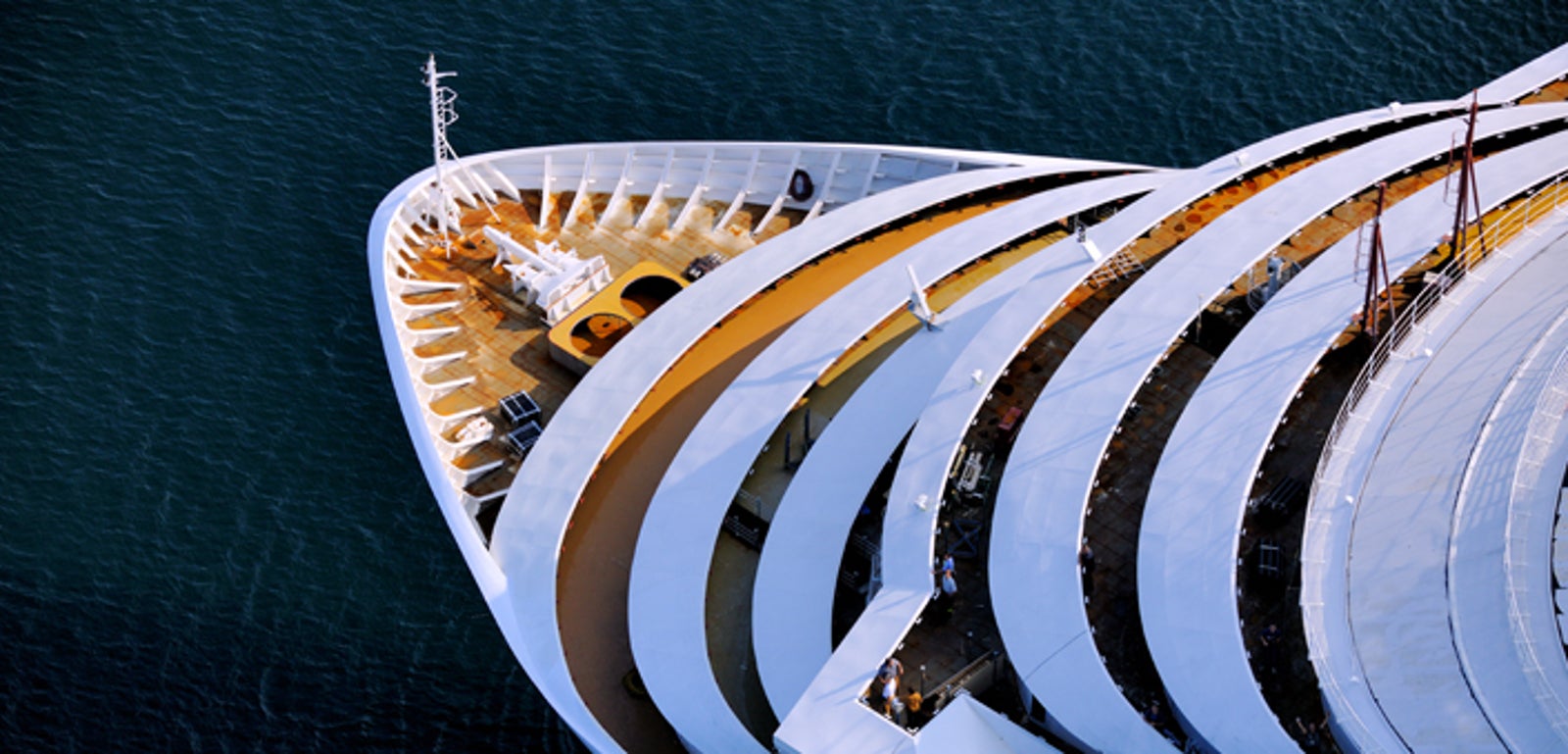 Fincantieri | Group - Business - Products - Cruise Ships - Carnival Dream: Overhead aerial view of the bow of large luxury cruise ship, elegant white design with stacked decks, ship docked in calm waters, highlights grandeur and modern architecture with extensive outdoor areas.
