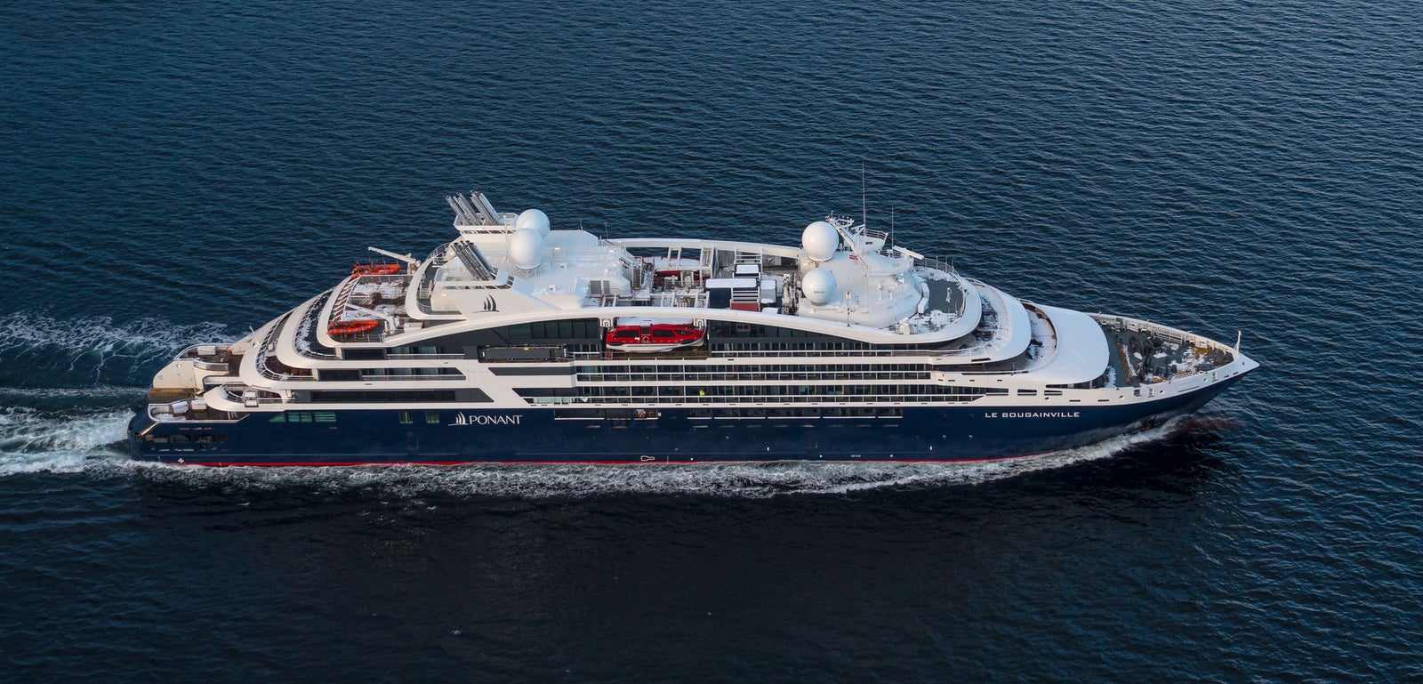 Fincantieri | Gruppo - Business - Prodotti - Navi da Crociera - Le Bougainville: Vista laterale della nave Le Commandant Charcot operativa in navigazione su mare aperto, scafo dal profilo lineare, ponti passeggeri multipli, cupole bianche e nome "Le Bougainville" ben visibile sulla fiancata.