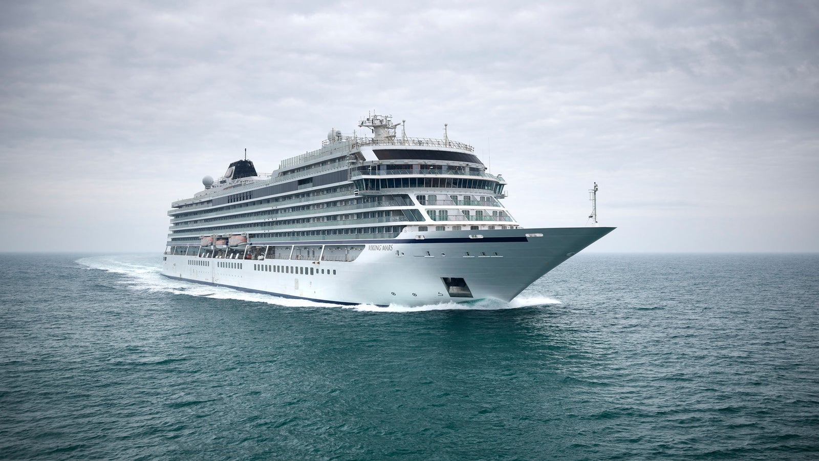 Fincantieri | Group - Business - Products - Cruise Ships - Viking Mars: Large modern cruise ship in operation, gliding through calm ocean waters under cloudy sky, multiple decks and sleek architecture, serene setting emphasizing ship’s grandeur and sea vastness.