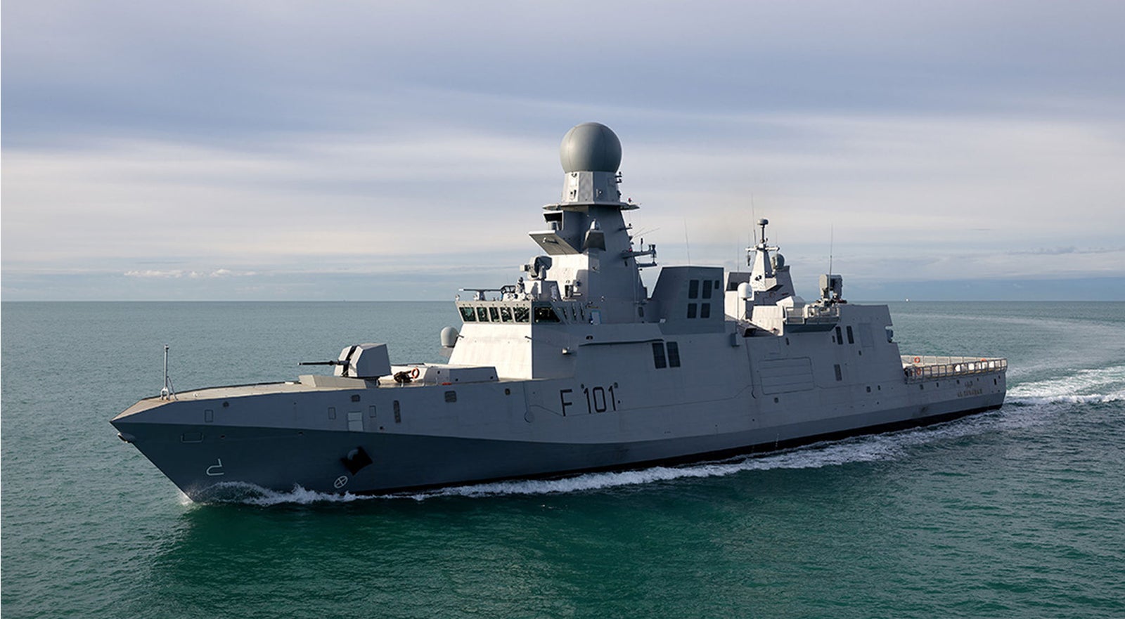Fincantieri | Gruppo - Società - Controllate e collegate - Fincantieri Services Doha: Nave militare moderna ‘F 101’ operativa in navigazione su acque calme sotto cielo nuvoloso, dotata di radar avanzati e design aerodinamico; ambiente oceanico evidenzia prontezza operativa e carattere marittimo.