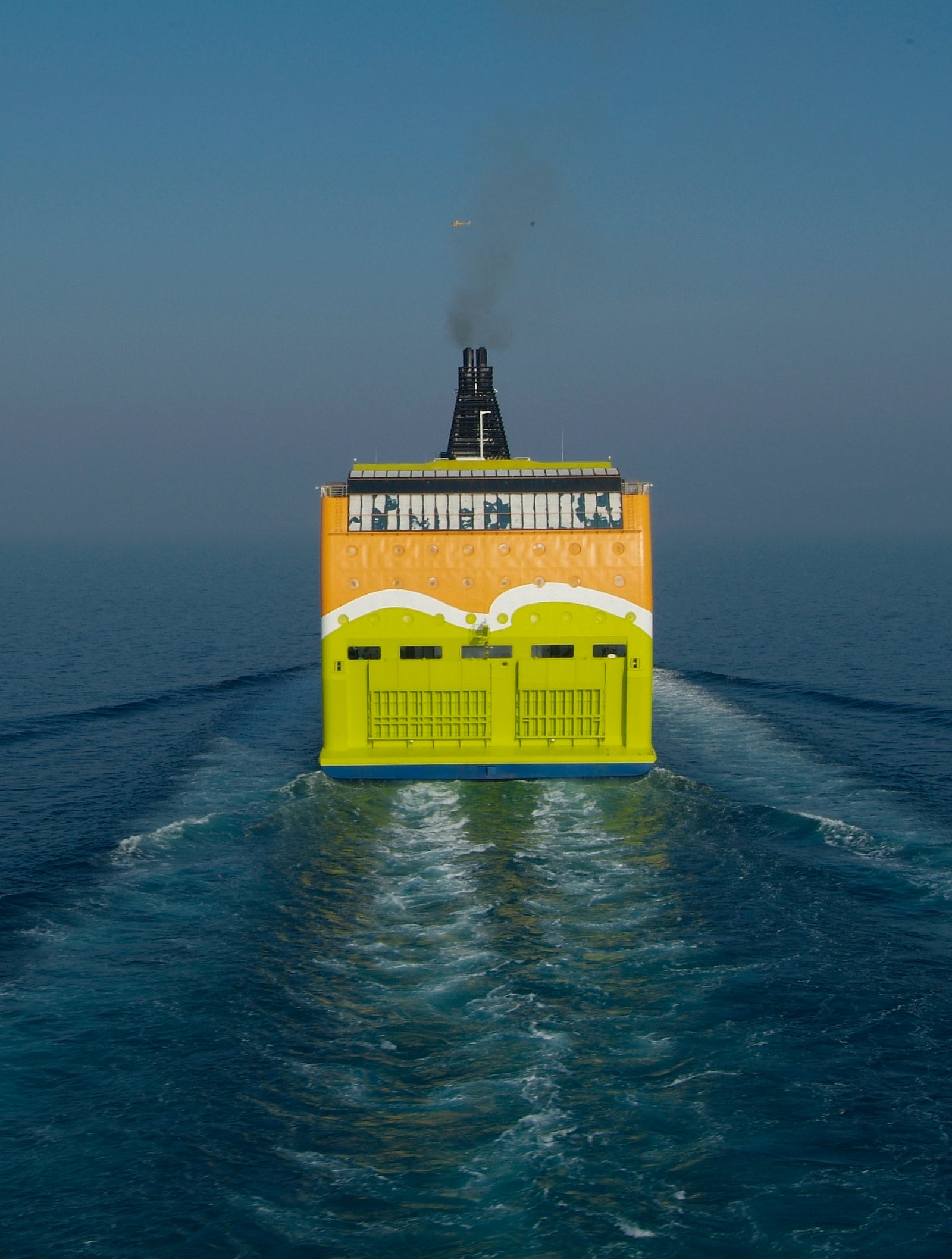 Fincantieri | Group - Business - Products - Ferries - Superstar: Vibrant yellow ferry in operation, bold graphics and visible text on stern, cruising through calm blue waters, clear sky.