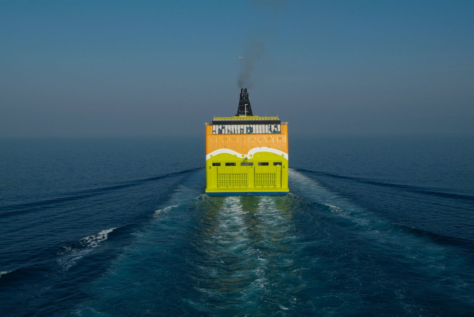 Prodotto - Traghetto Tallink Superstar: Vista posteriore della nave operativa in navigazione, scafo giallo vivace con grafiche e testo evidenti, ambiente marittimo sereno e oceanico.